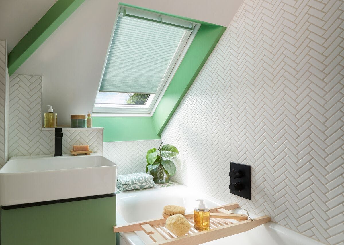 Mint‑green and white bathroom with a skylight window fitted with a pale green pleated blind, featuring herringbone tiles and soft fresh colours.