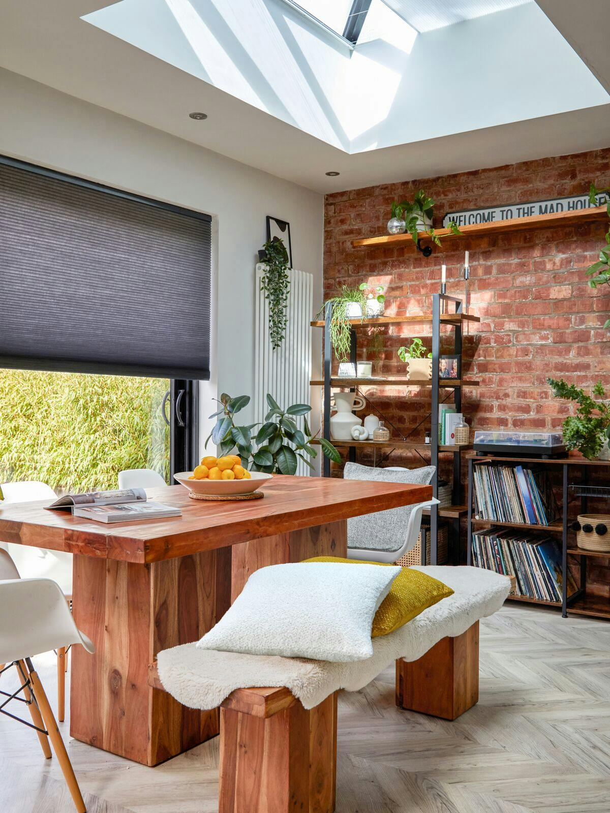 Dining area with door and window combination dressed in blue-grey duette blinds partially lowered, rustic wooden table and benches underneath a roof lantern window.