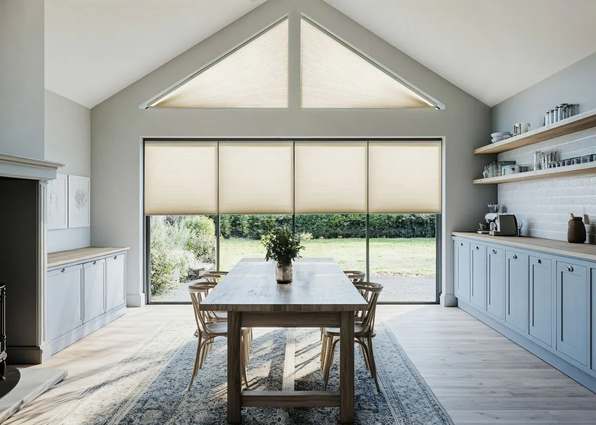 Modern light-filled kitchen-diner with large gable end windows fitted with sand coloured duette blinds.