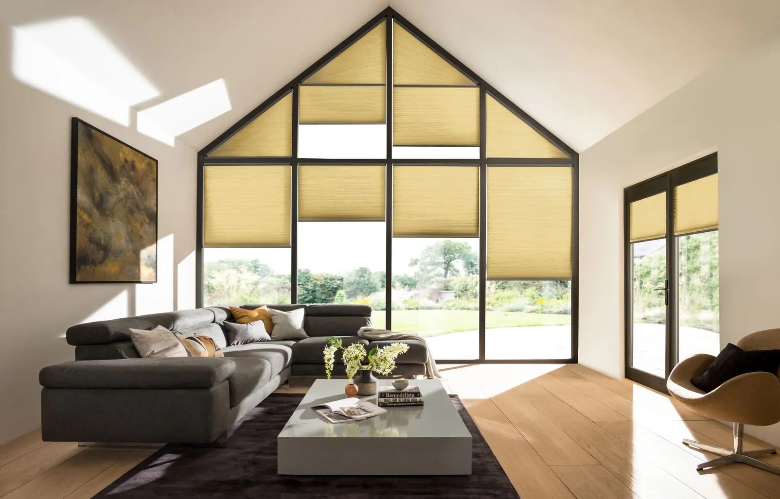 Living area with grey sofa and low table on a rug over a wooden floor with gable end window dressed in pale caramel duette blinds at varying levels.