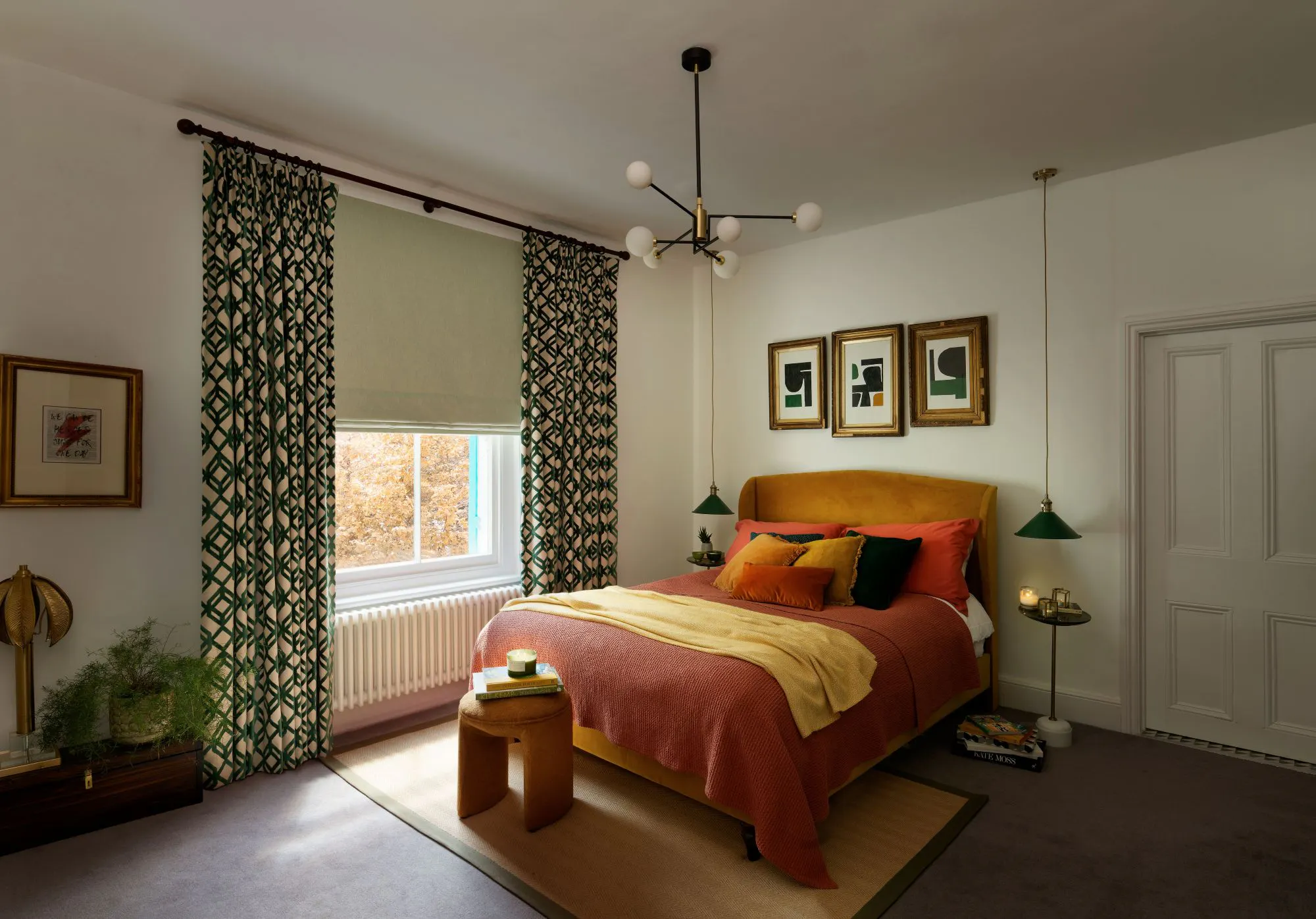 A comfortable bedroom features a bed with colorful pillows and a throw blanket, accompanied by modern lamps and artwork. The room is illuminated by a window with patterned curtains.