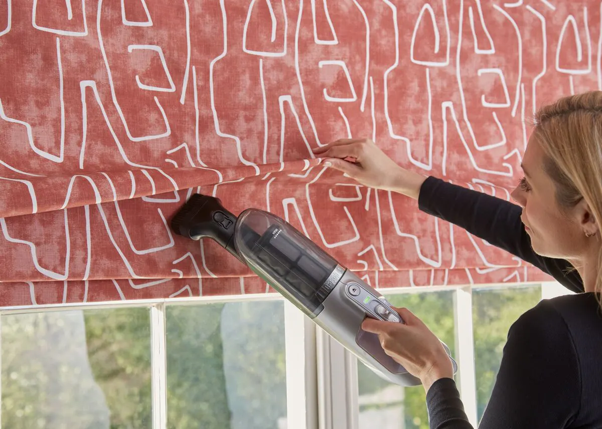 lady with blonde hair using a machine to clean a red roman blind with white patterns on it