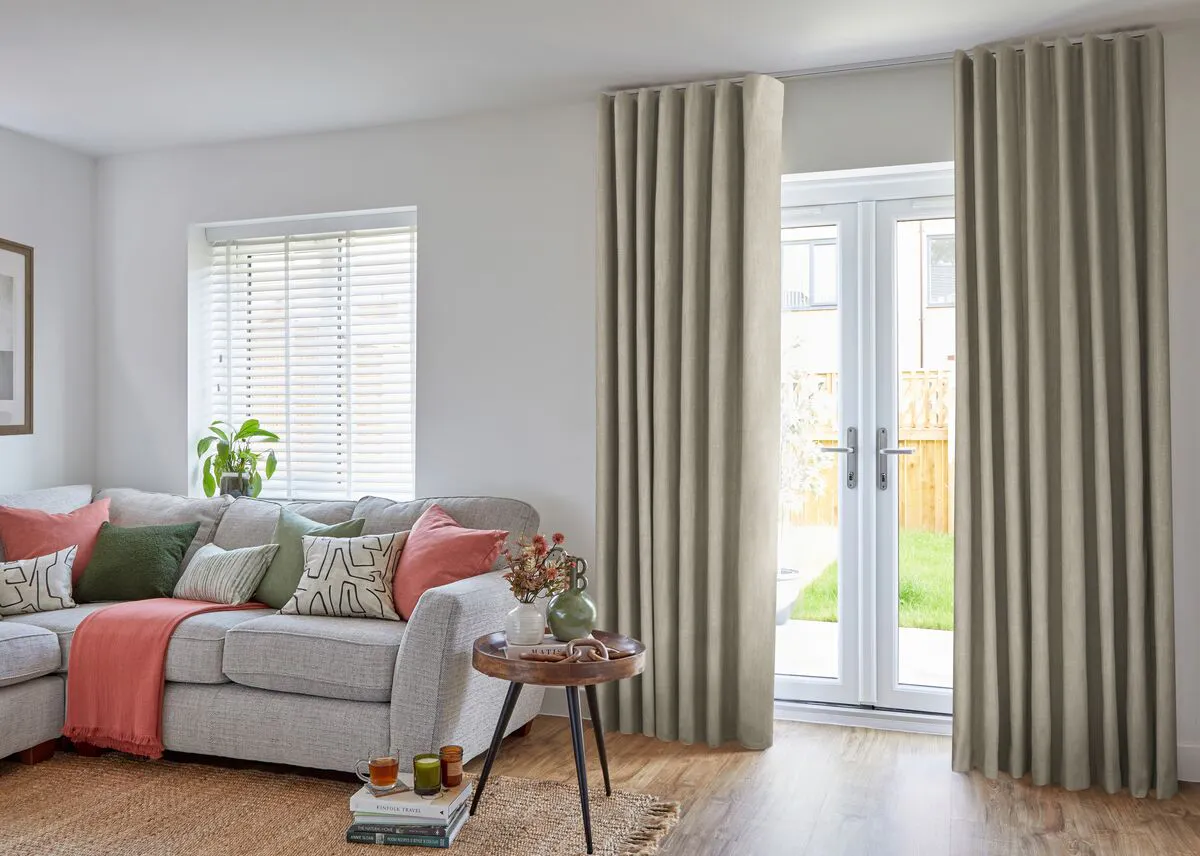 Living room with glazed French doors framed by neutral curtains, opening to a garden and filling the space with soft natural light.