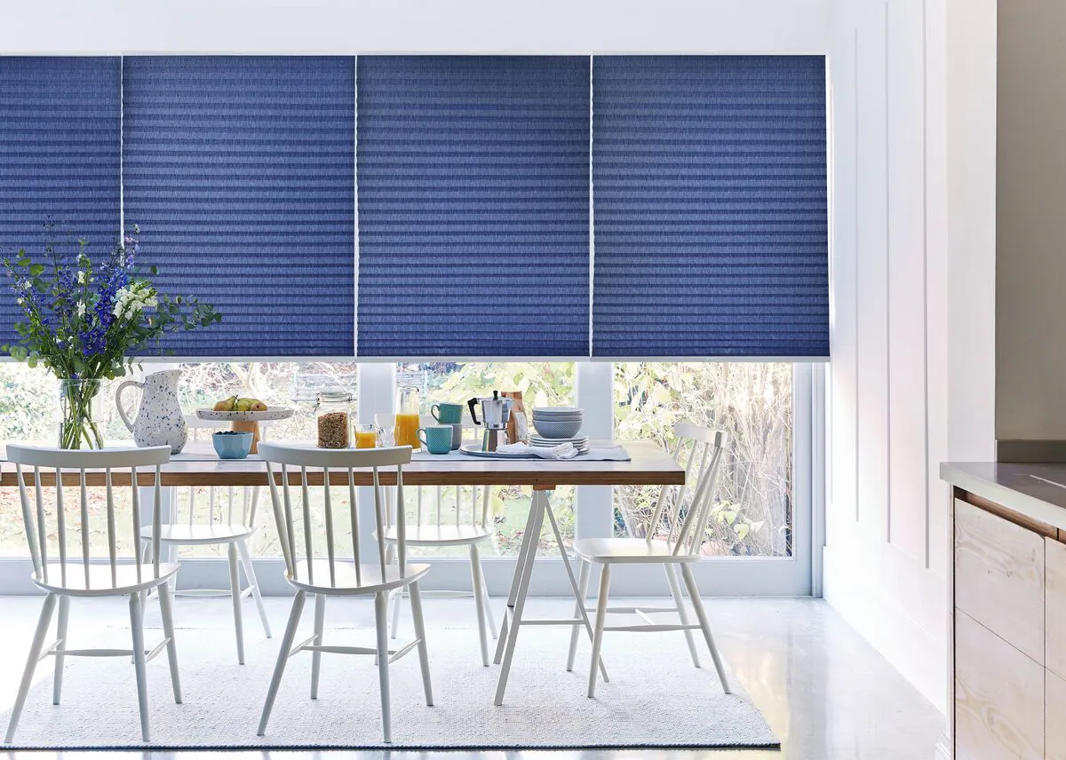 Dining room with large windows dressed with blue Pleated blinds, overlooking a bright garden.