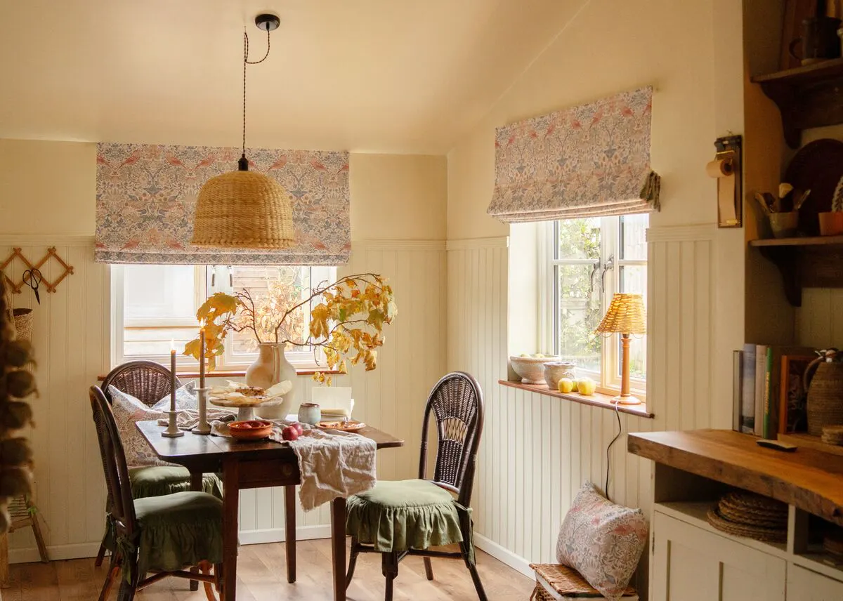 A cosy dining area with two patterned Roman blinds over bright windows, softly lighting the room with a warm, homely glow.
