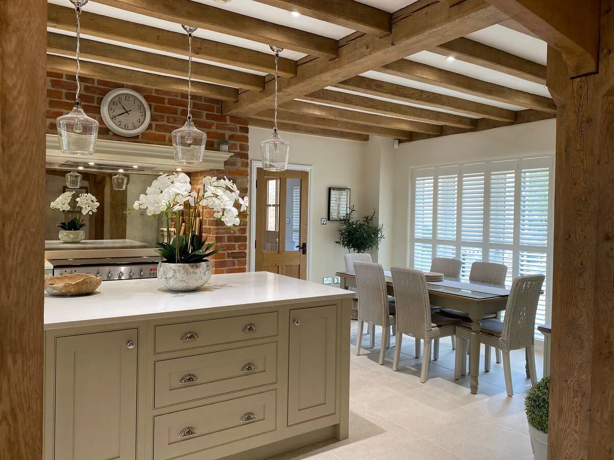 A bright kitchen-diner with a large window dressed in white full-height shutters letting in soft natural light.