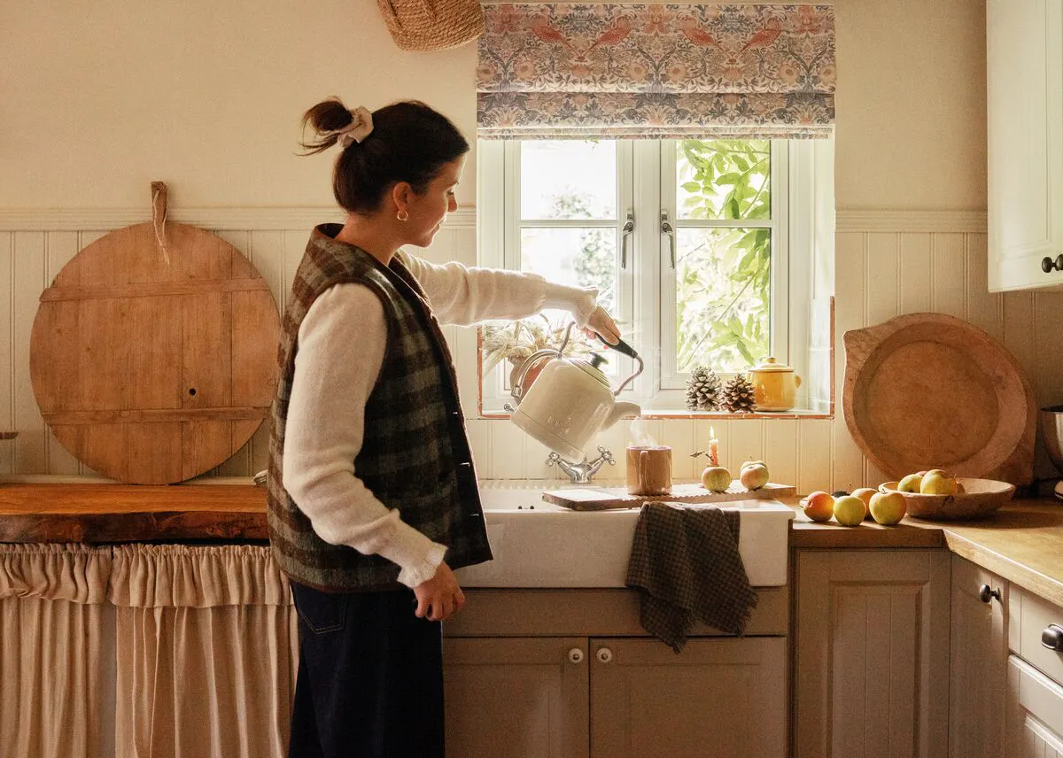 A small kitchen window dressed with a patterned Roman blind, letting in soft light above the sink area.