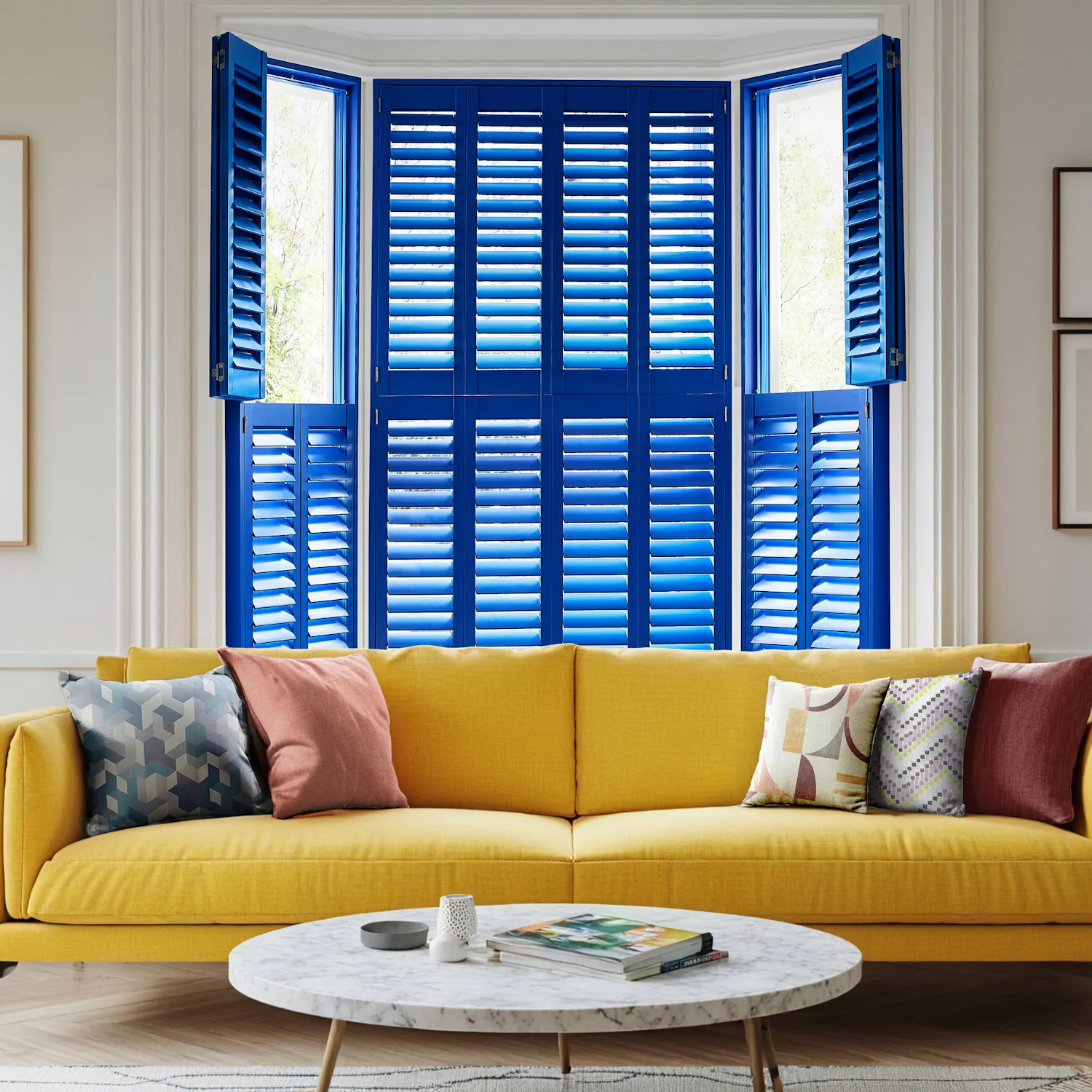 A bright living room with bold cobalt blue shutters in a bay window, a mustard yellow sofa and colourful geometric cushions against neutral