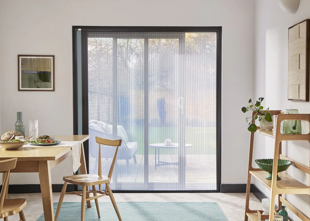 Bright dining area with wide patio doors fitted with a Fly Screen, opening to the garden and filling the room with natural daylight.