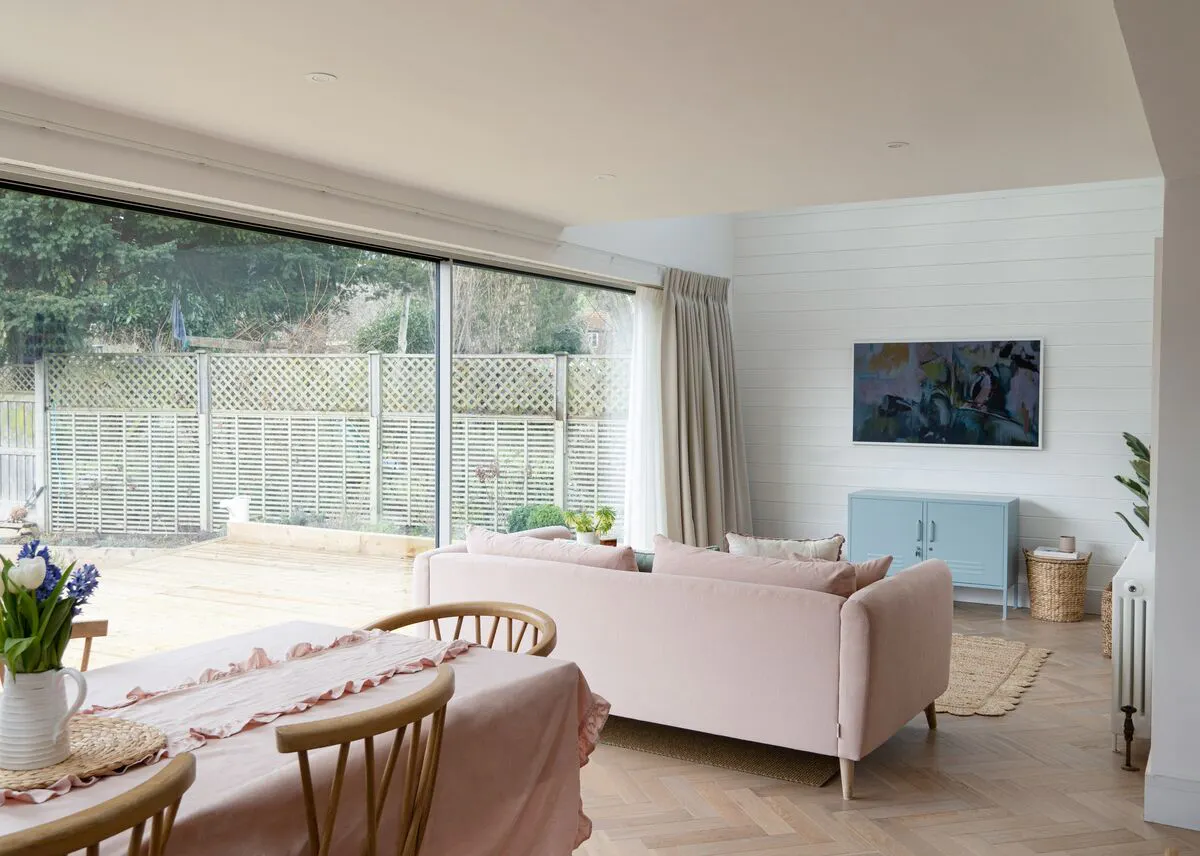 Open‑plan living space with wide sliding glass doors and soft curtains, opening onto a garden and filling the room with natural light.