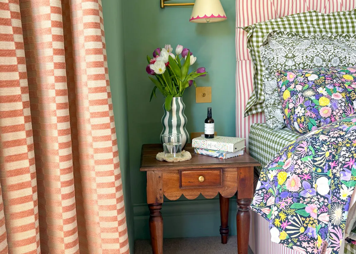 Close in on terracotta and cream gingham curtains in bedroom with green walls, bed in pink and white stripes, floral bedding.