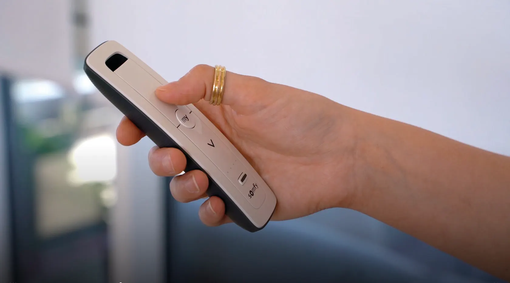 Hand holding a slim remote control with raised buttons, used to operate blinds in a modern home setting.
