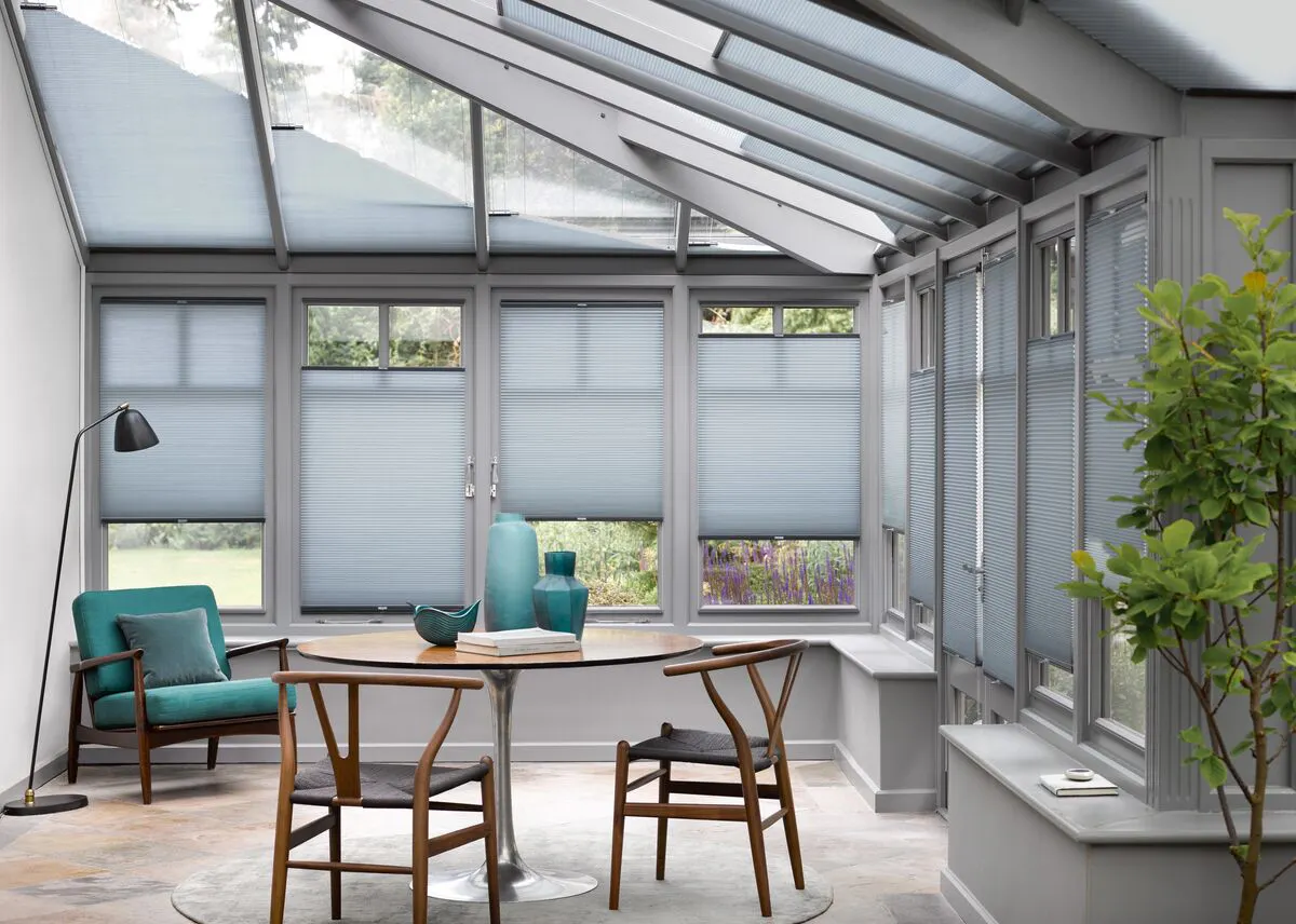 Bright conservatory with large windows fitted with Pleated blinds, filling a stylish dining space with soft natural light.
