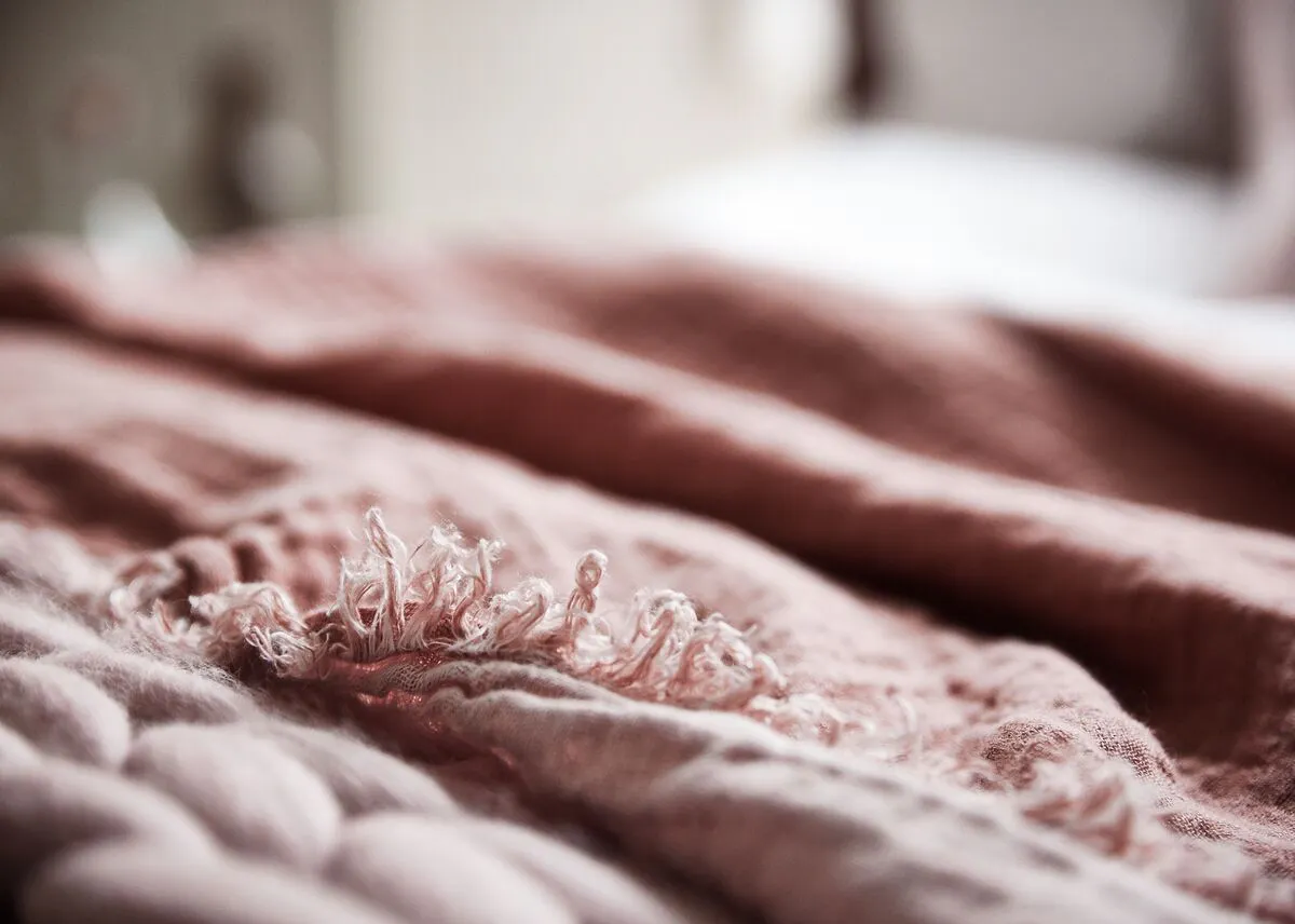 A close-up of layered blush pink bedding shot in soft focus with a gently blurred background.