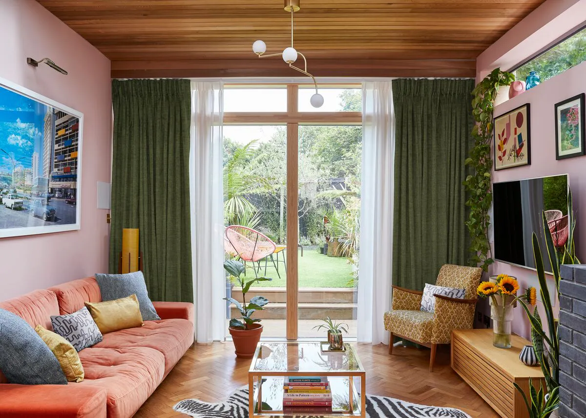 Large glazed doors framed with sheer Voile curtains and green curtains, opening the living room to garden views and filling the space with light.