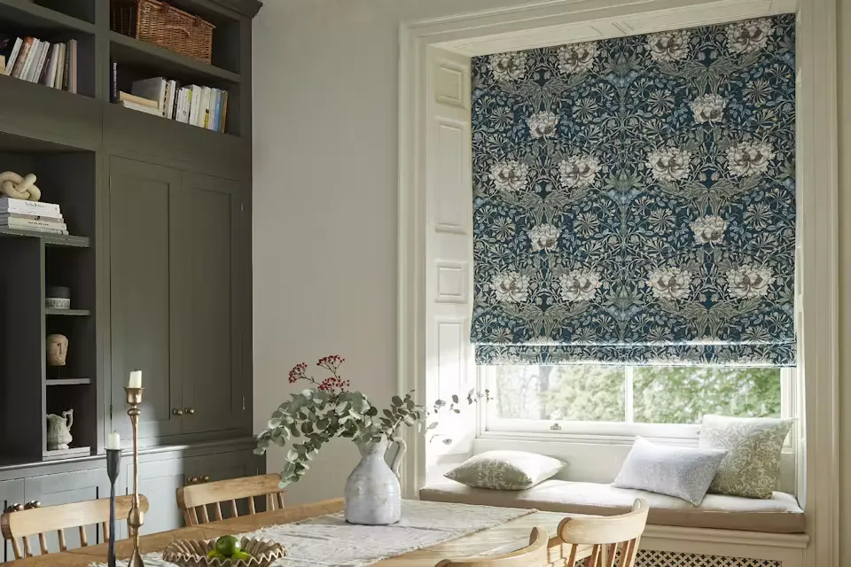 Living room with floor-to-ceiling windows dressed in heavy curtains, opening onto a garden and centred around a wood-burning stove.
