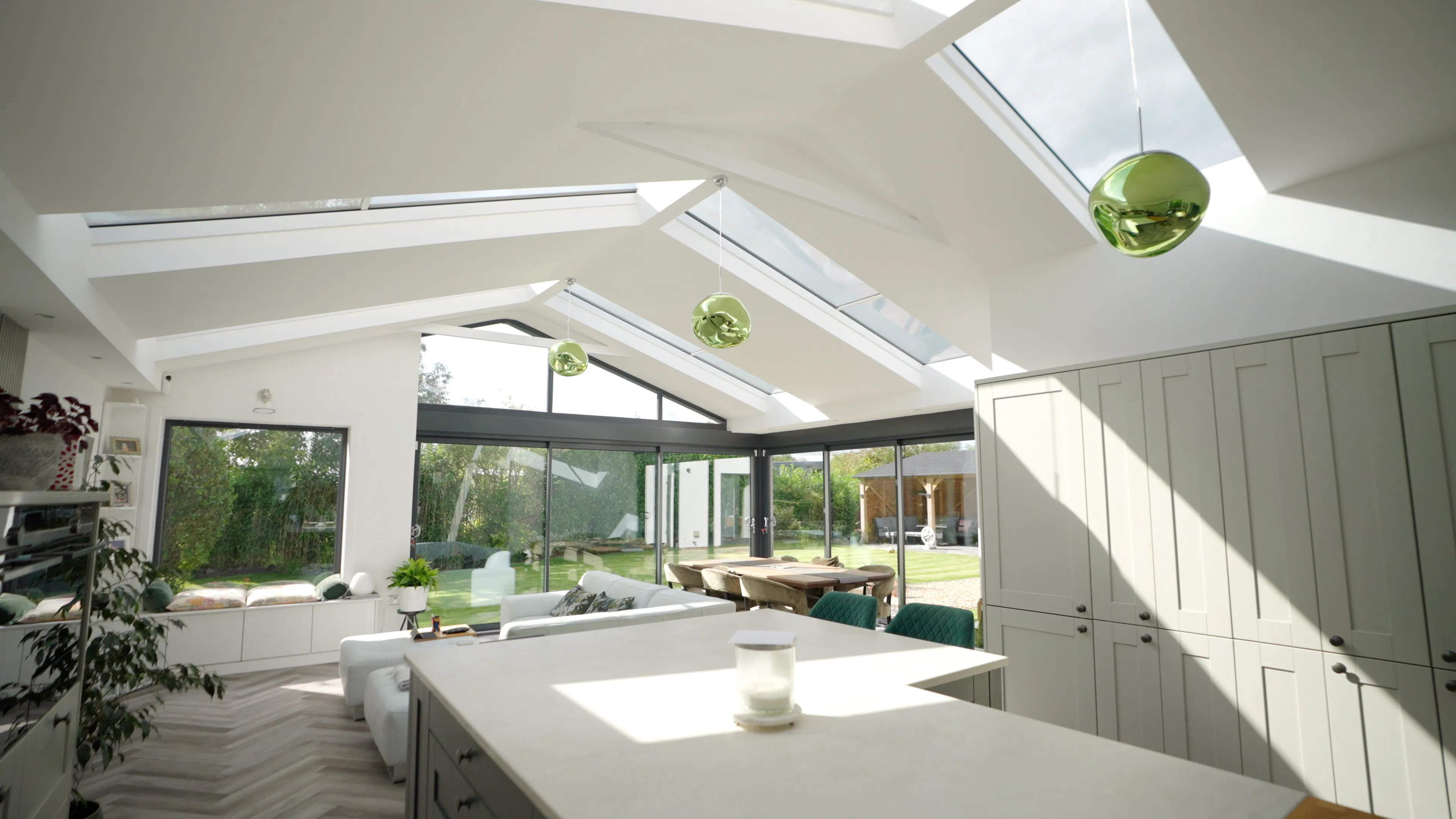 Bright open-plan interior with large roof windows and full-height glazing, flooding the dining and living space with natural light.