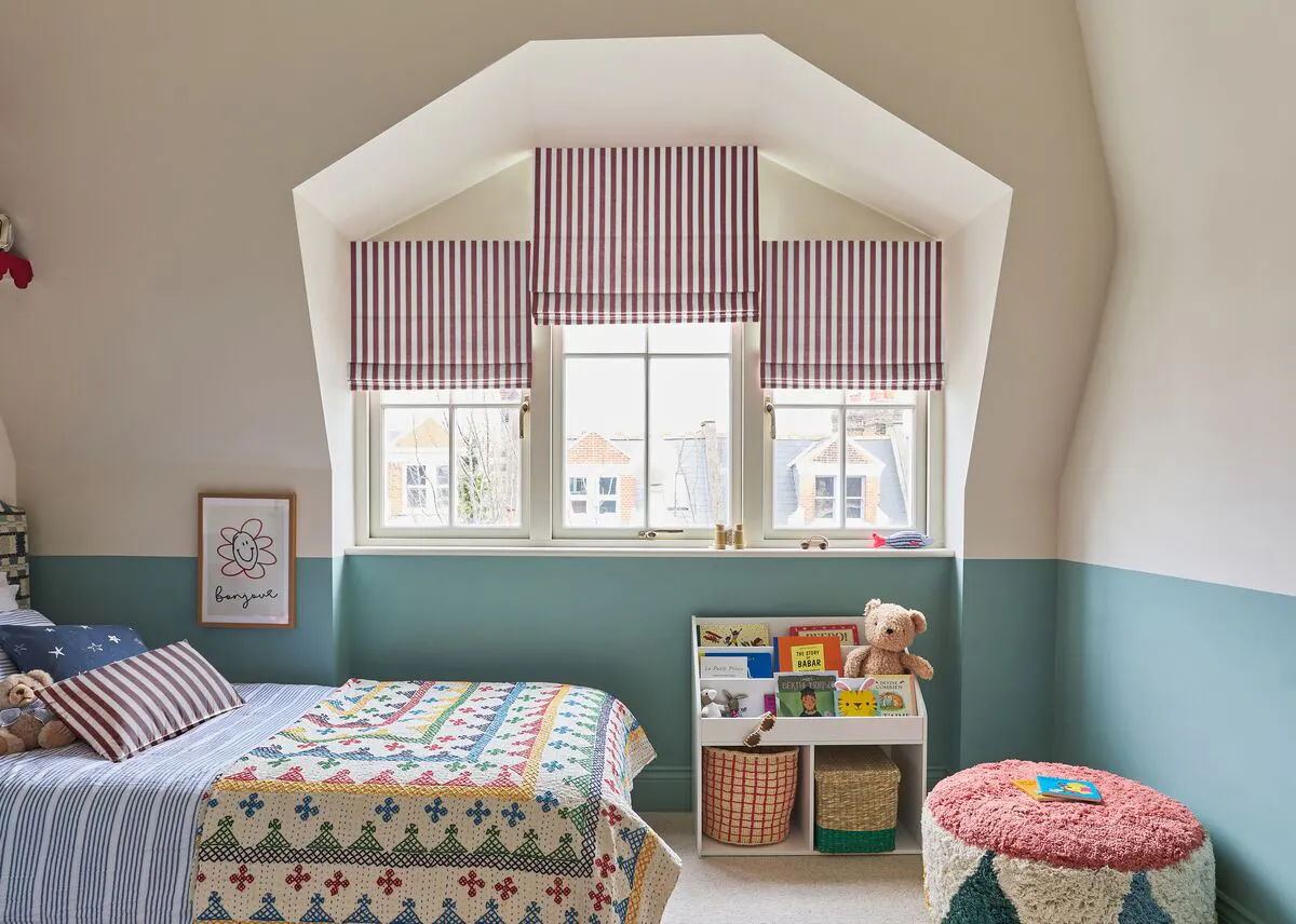 Red and white striped Roman blinds dress a dormer window in a bright children’s bedroom with teal walls and playful furnishings.