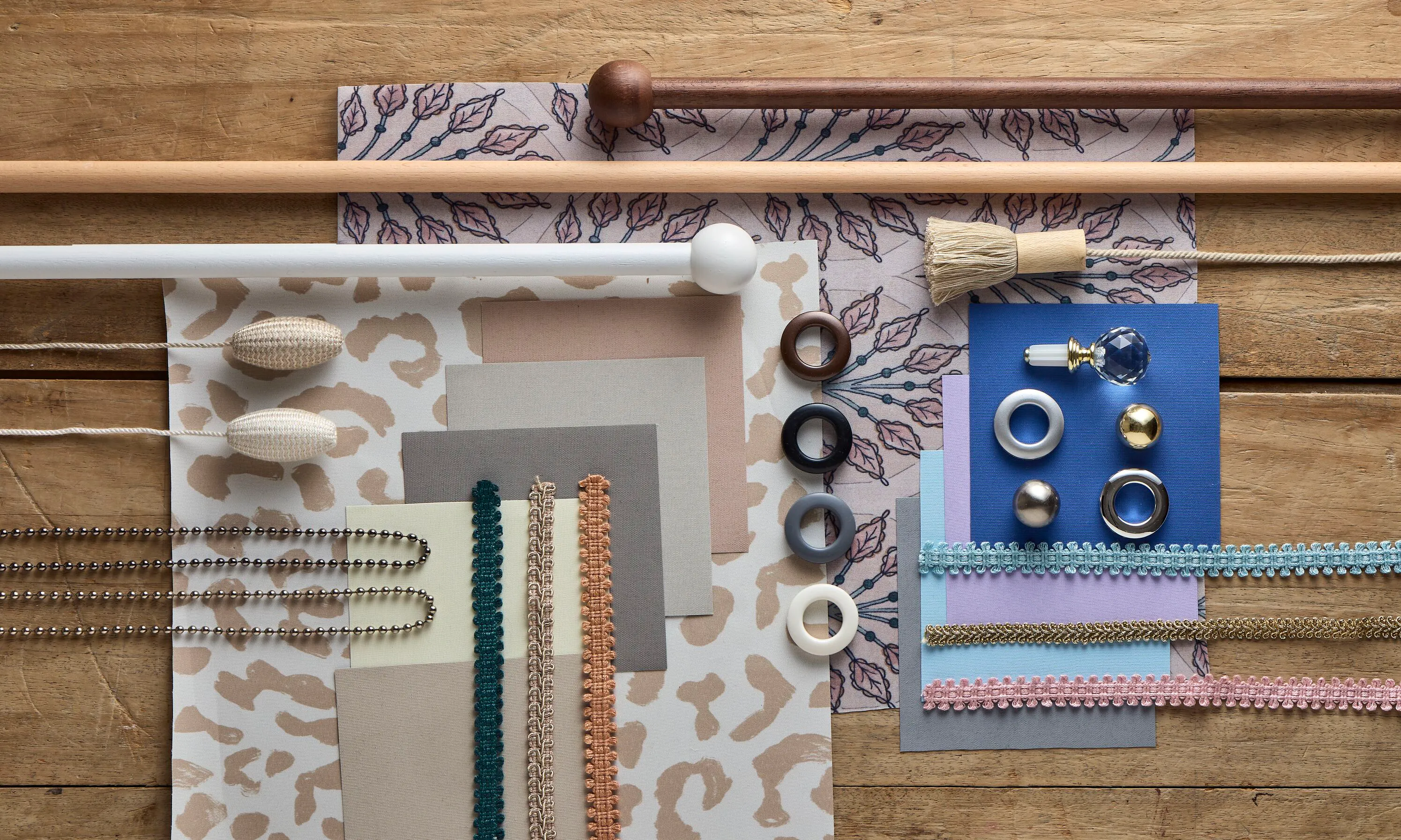 A flat lay of animal print and floral fabric samples, trimmings, pole finials and eyelet rings arranged on a wooden surface.