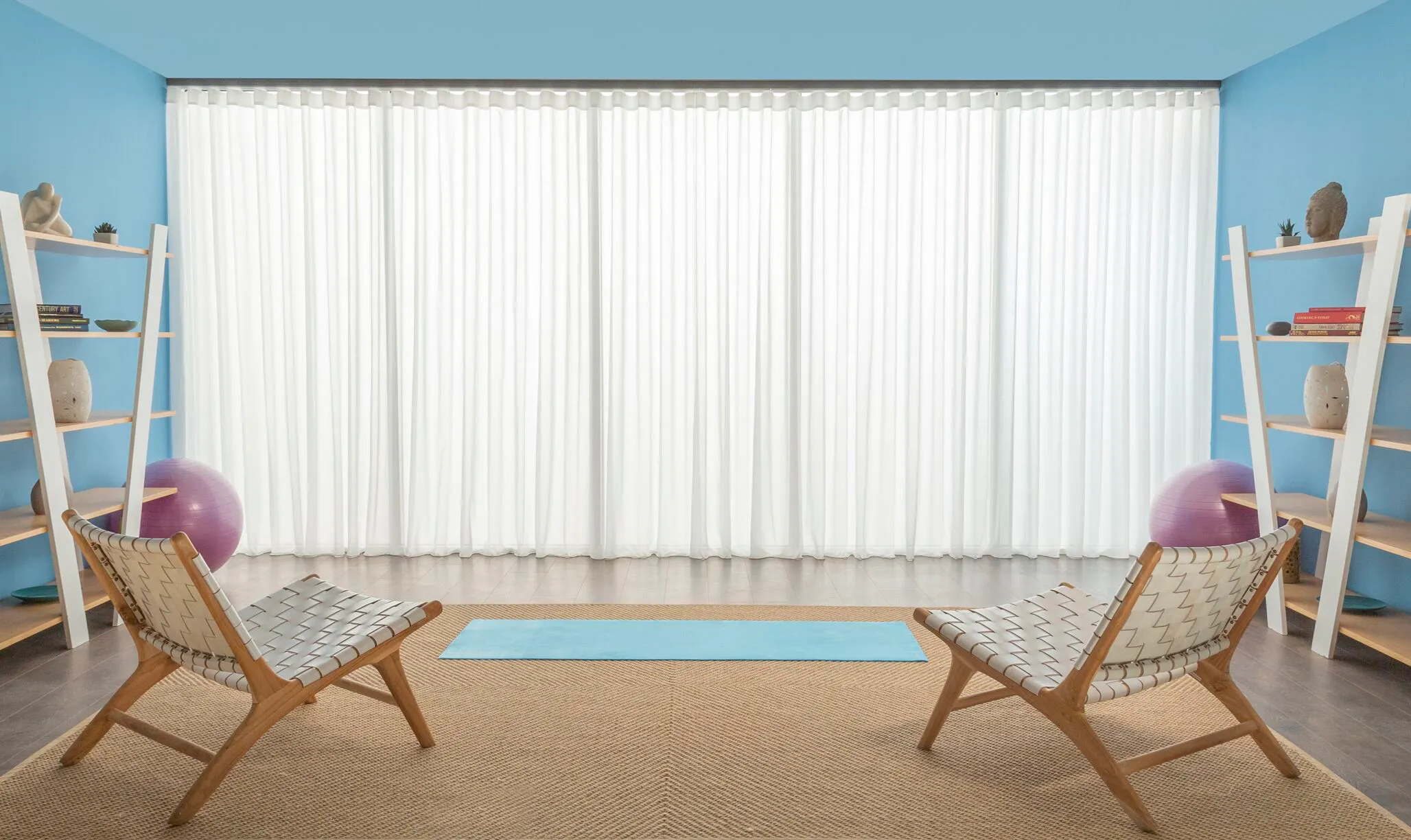 Bright room with floor-to-ceiling window dressed in sheer white Voiles, flanked by blue walls, lounge chairs and shelving.