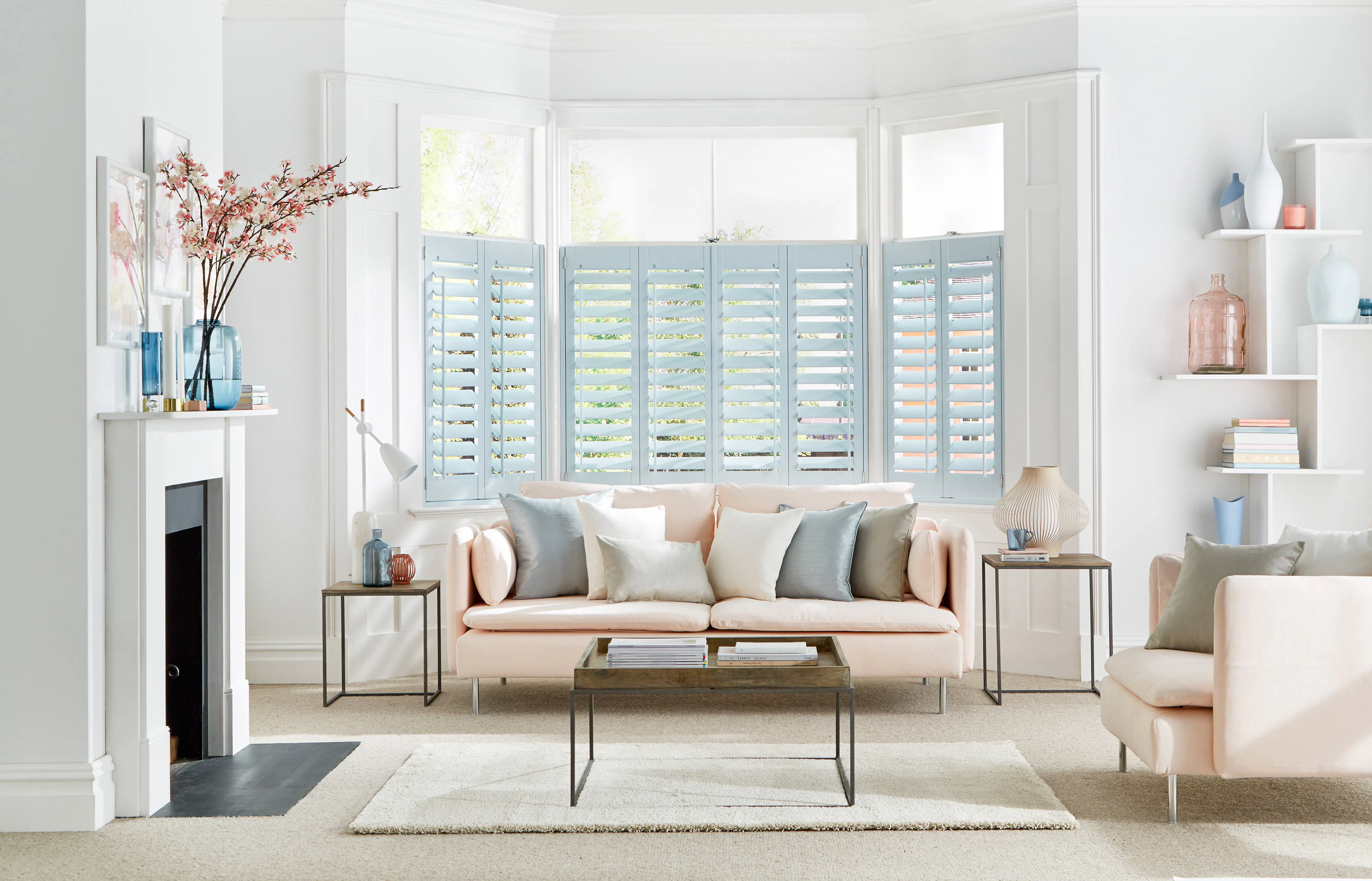 Light living room with a bay window fitted with soft blue shutters, framing the sofa and gently filtering daylight into the space.