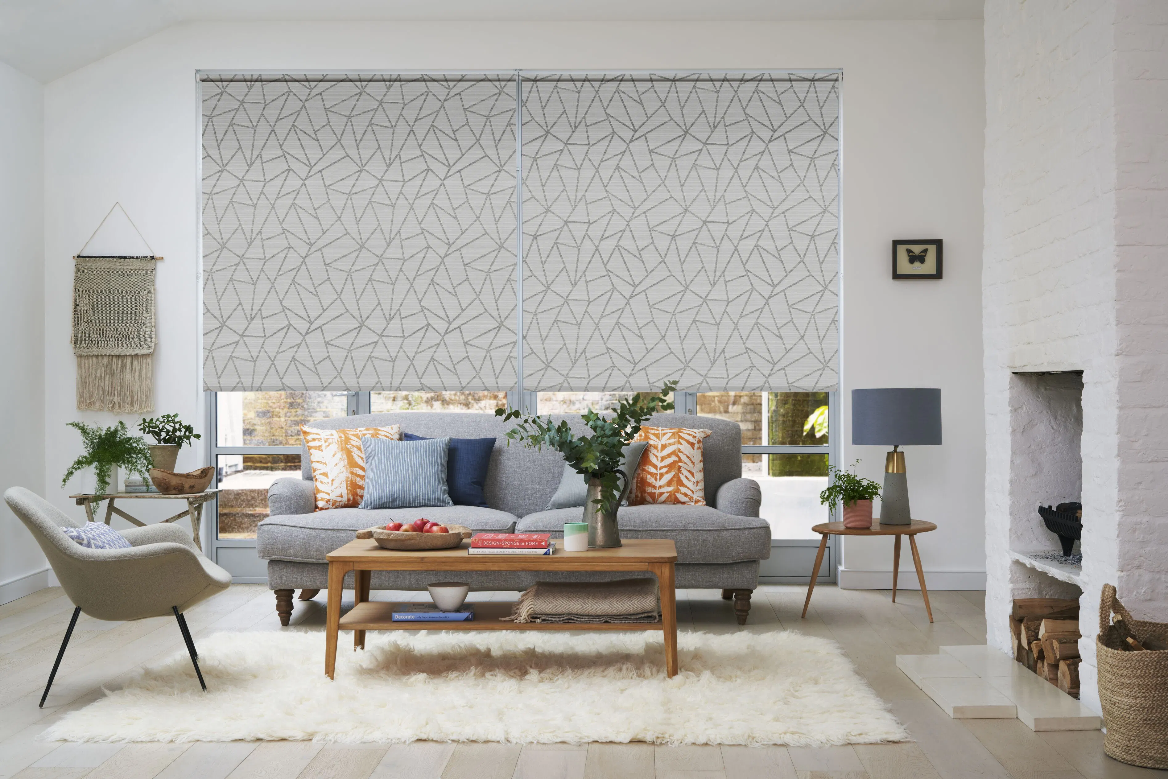 Two large patterned Roller blinds cover floor-to-ceiling windows behind a sofa, filtering daylight into a bright, contemporary living room.
