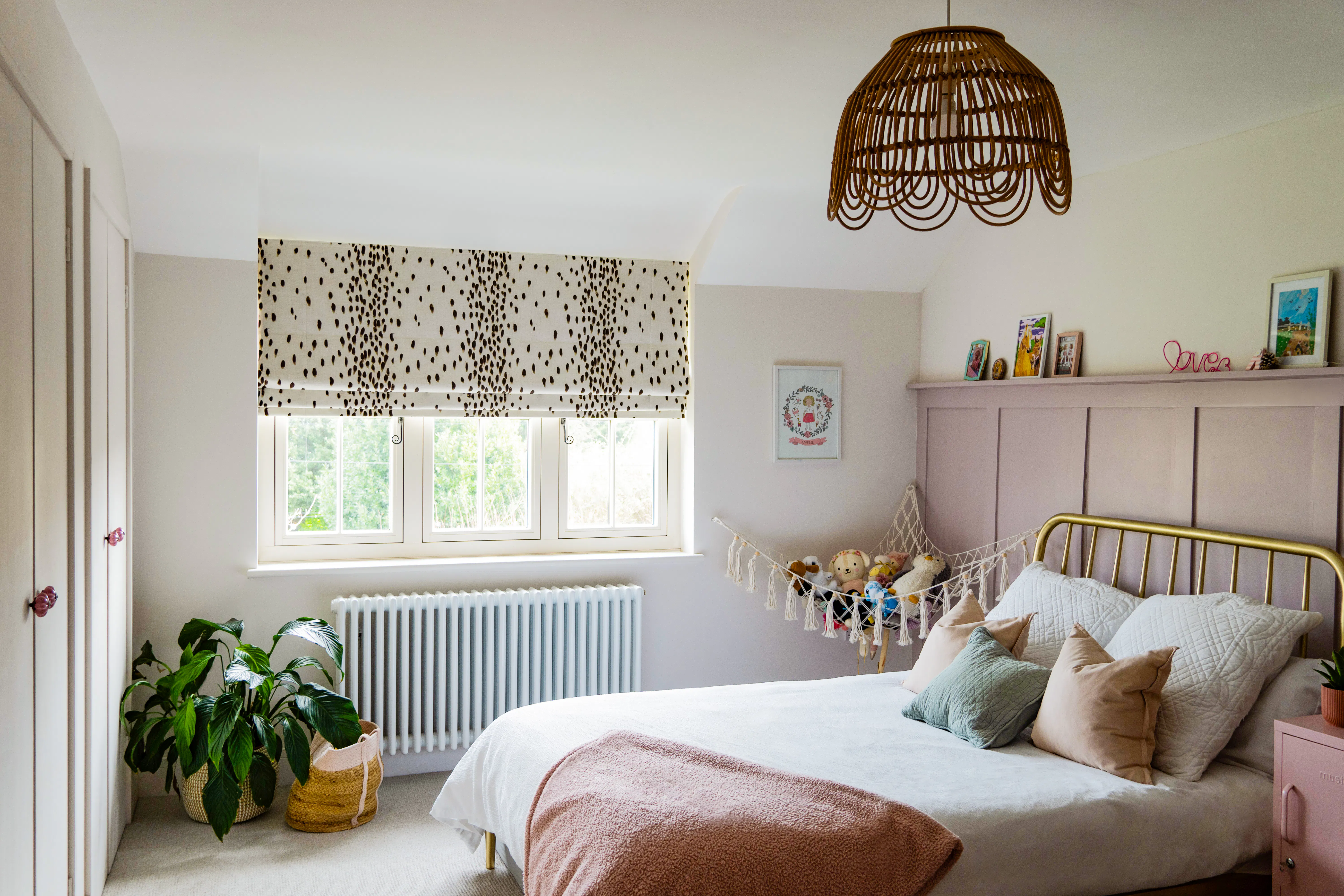A boho-style teen bedroom with a Dalmatian-print Roman blind, panelled pink wall and a rattan pendant light.