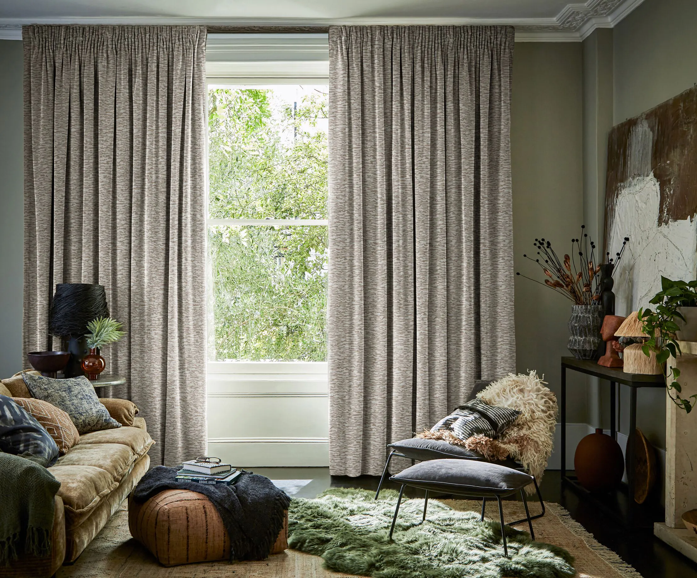 Large window framed by full-length textured curtains, bringing daylight into a cosy living room with layered furnishings and soft neutral tones.