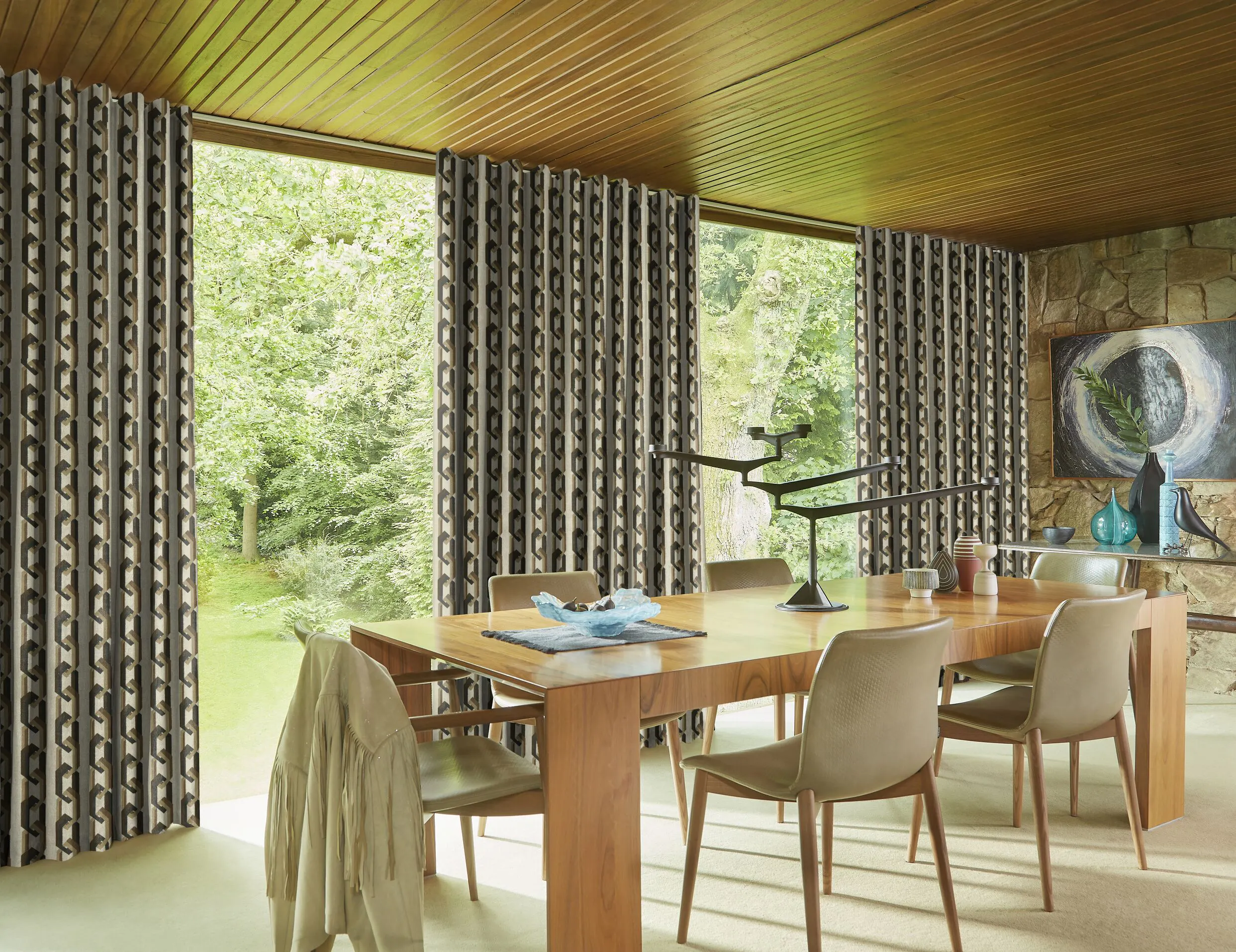 Floor-to-ceiling patterned curtains frame large garden-facing windows in a contemporary dining room with a wooden table and chairs.