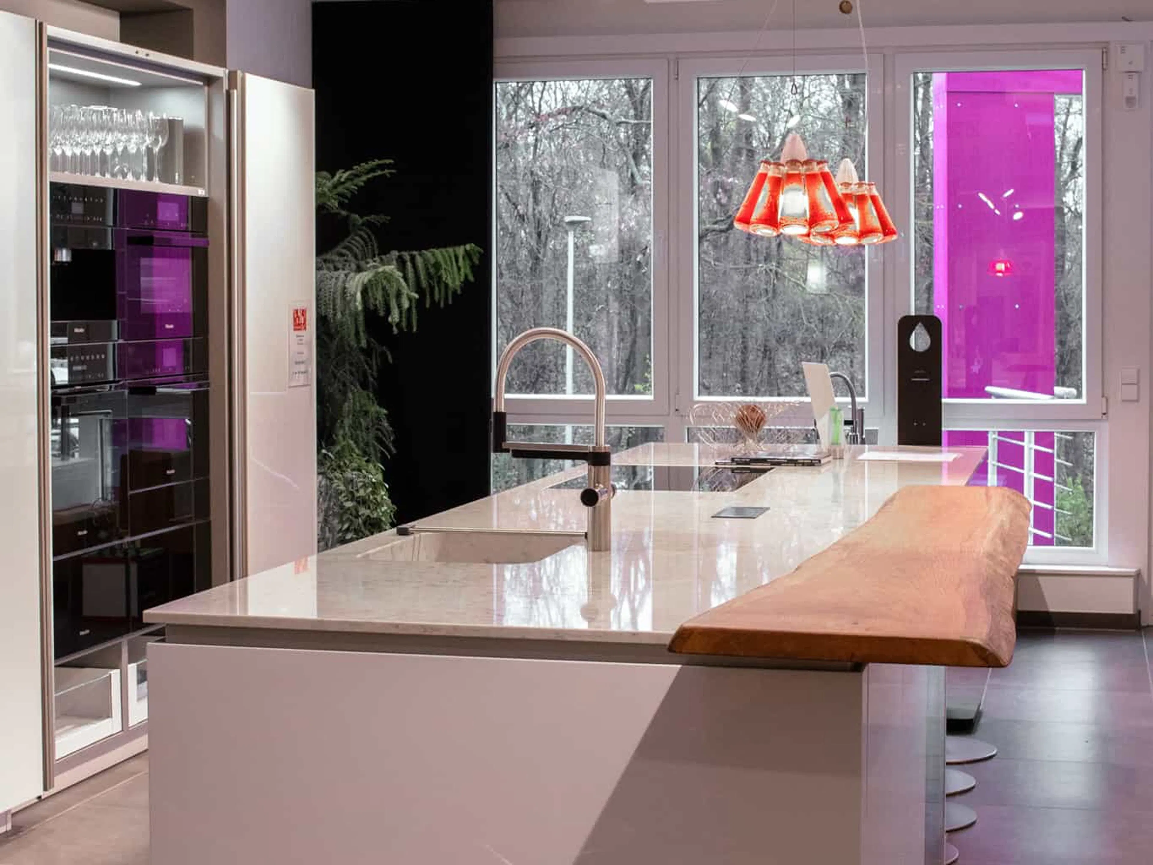 Referenz Hiller Küchenstudio: Moderne Kochinsel mit heller Arbeitsplatte und integrierter Massivholztheke vor großen Fenstern.