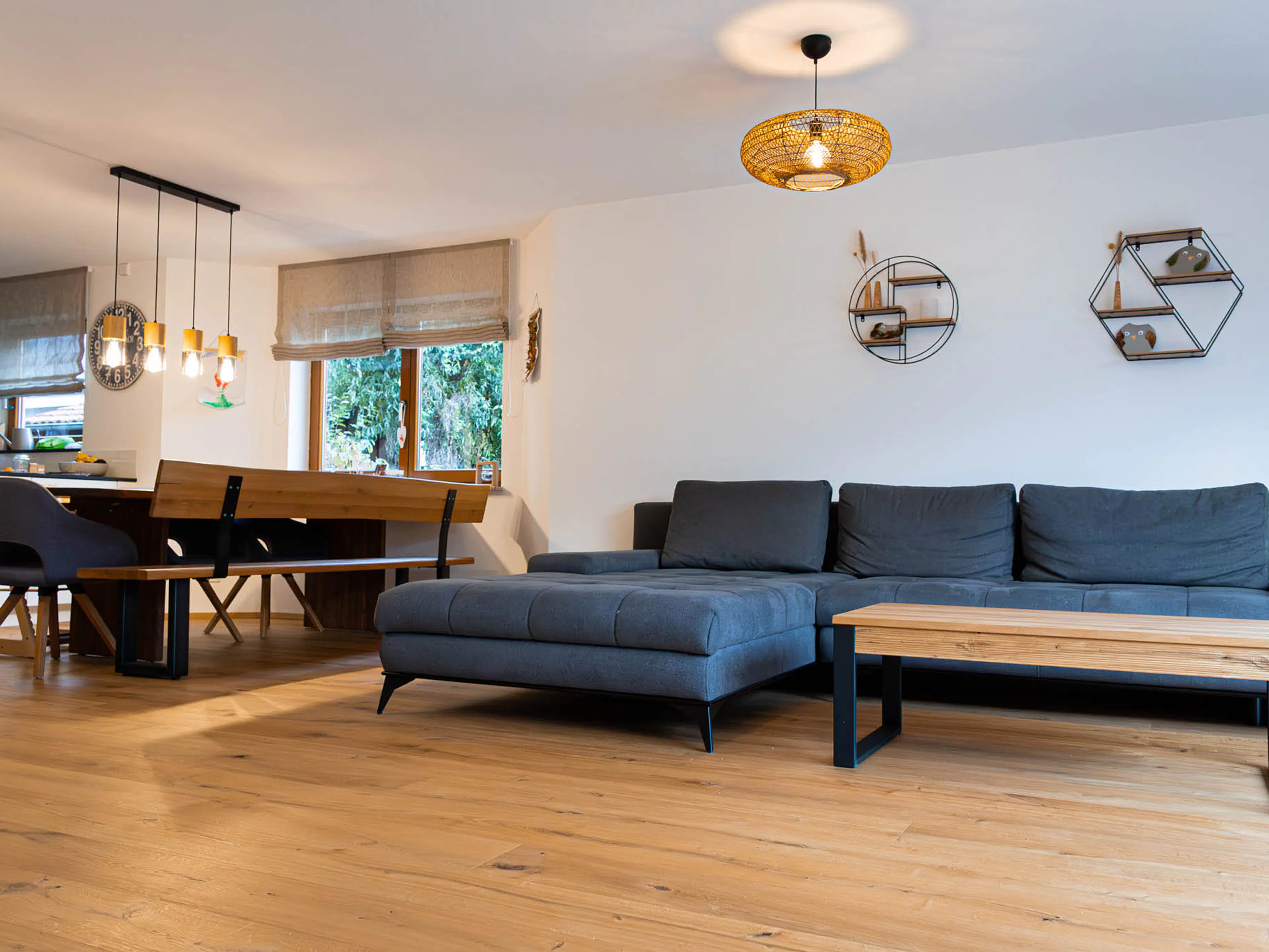 Referenzprojekt Parkett Saussele: Modernes Wohnzimmer mit hochwertigem Holzparkett, grauem Sofa und Essbereich.