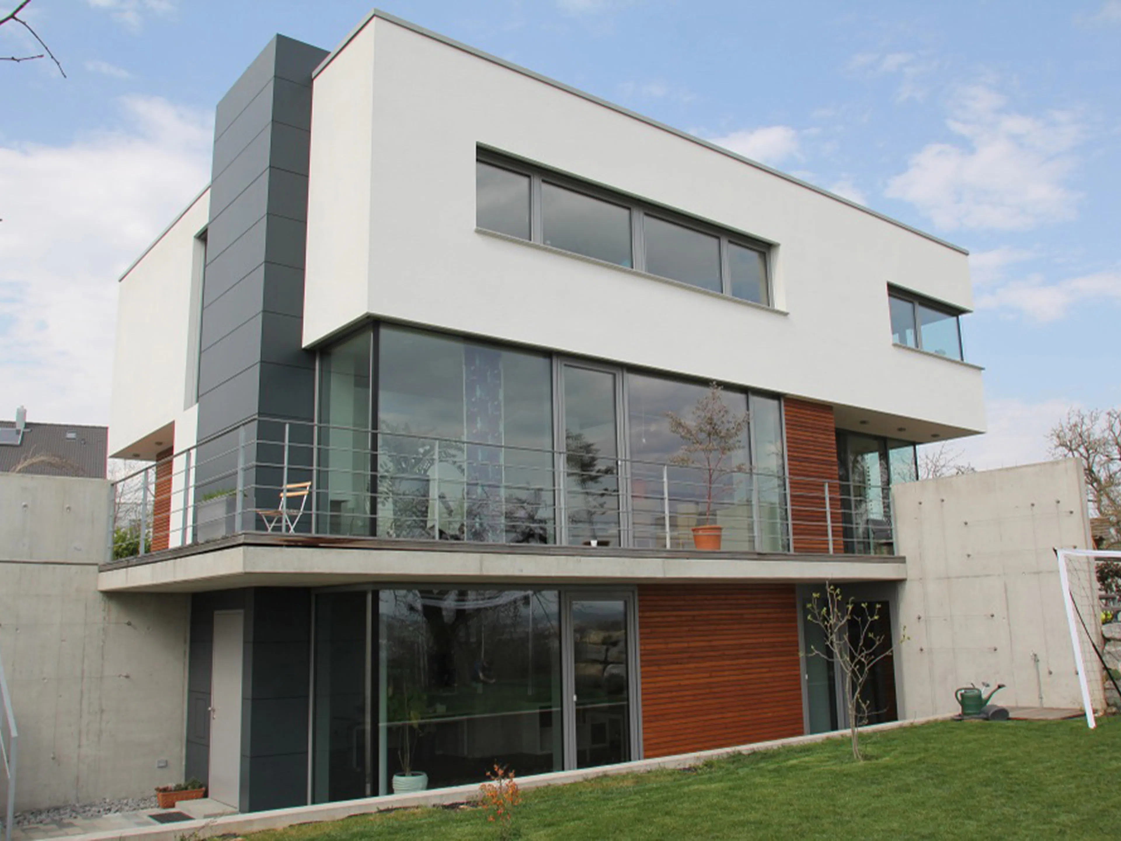 Modernes Wohnhaus im Bauhaus-Stil mit weißem Putz, Holz- und Grauelementen, fachgerecht vom Döbele Stuckateurbetrieb umgesetzt.