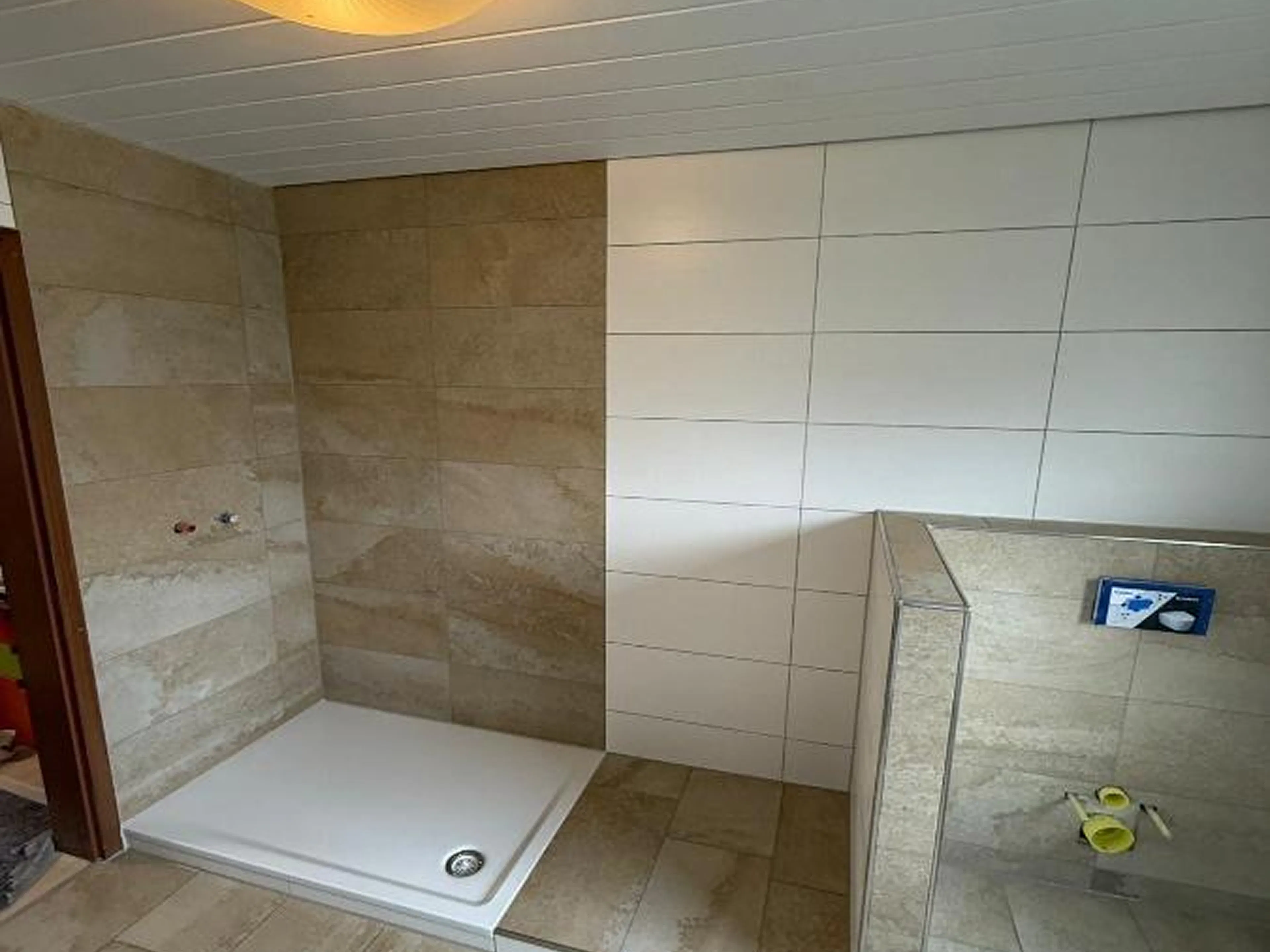 Badsanierung durch Fliesen Kurz: Fachgerecht verlegte beige und weiße Wand- und Bodenfliesen rund um eine neue Duschwanne.