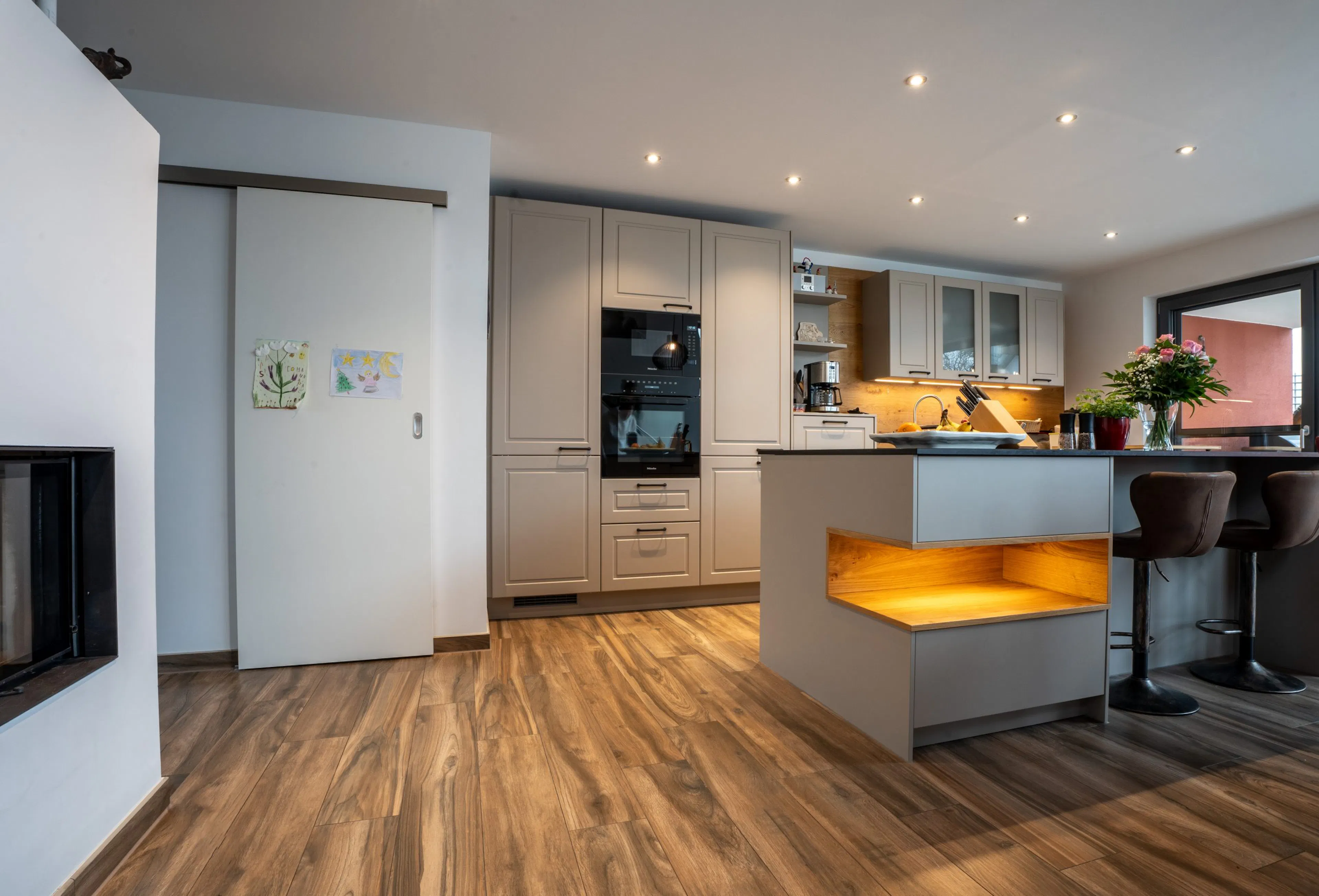 Referenz Hiller Küchenstudio: Moderne Küche in Taupe mit beleuchteter Kochinsel-Nische und Holzboden in Hessigheim.