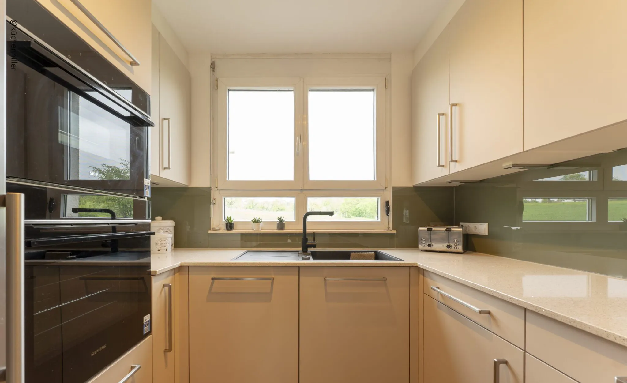 Küchenplanung von Hiller Küchenstudio: Funktionale U-Küche in Beige mit schwarzer Spüle direkt vor dem Fenster in Ingersheim.