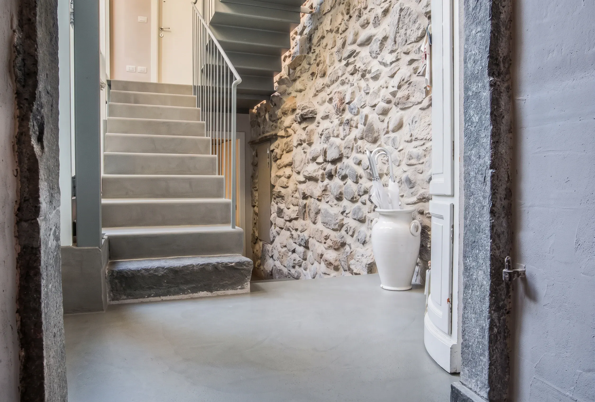 Referenz Döbele Stuckateurbetrieb: Moderne Treppe und fugenloser Boden neben einer historischen Natursteinwand im Keller.