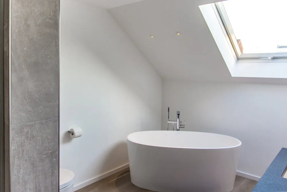 Modernes Badezimmer von Döbele Stuckateurbetrieb: Freistehende Badewanne unter Dachfenster mit grauen Wandplatten.