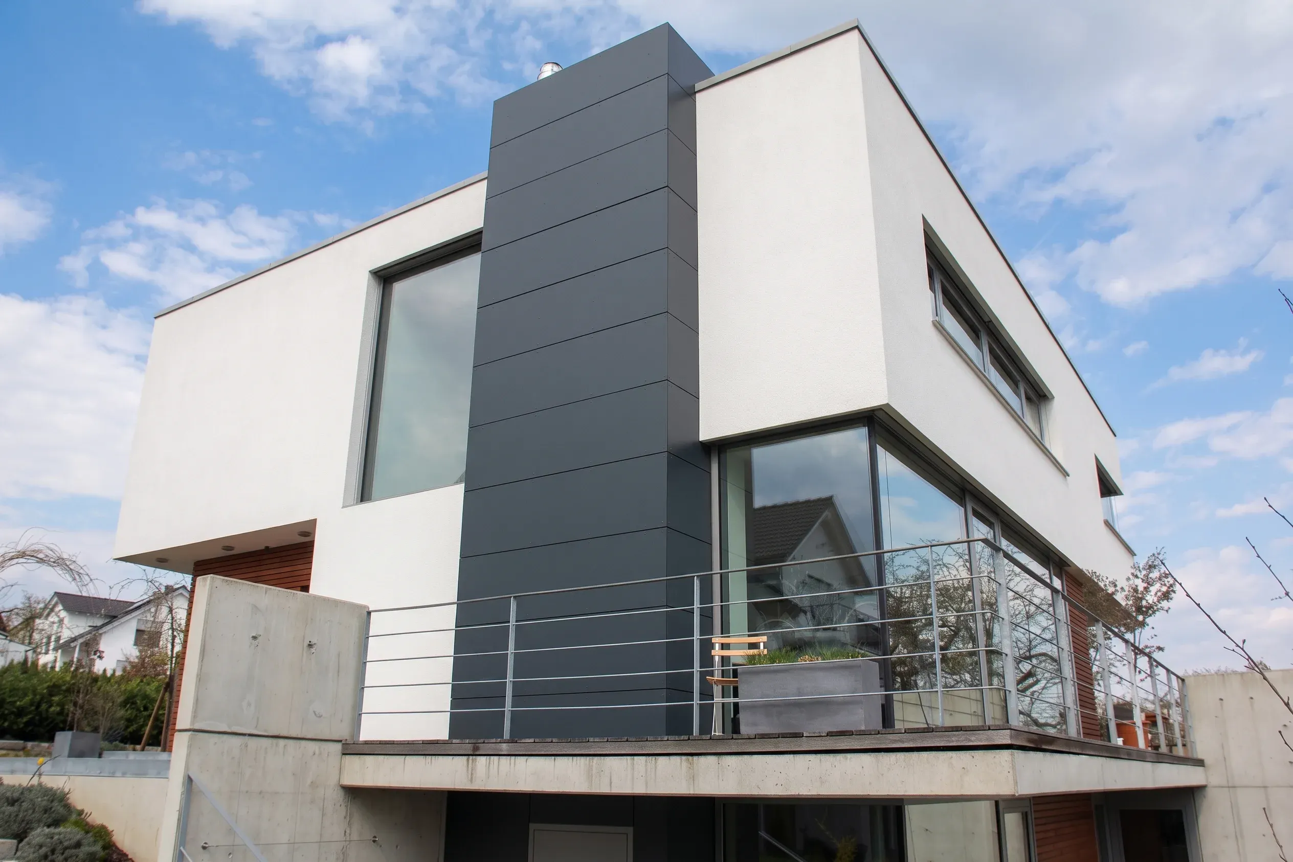 Fassadengestaltung durch Döbele Stuckateurbetrieb: Modernes Wohnhaus mit weißem Edelputz und dunklen Fassadenplatten.