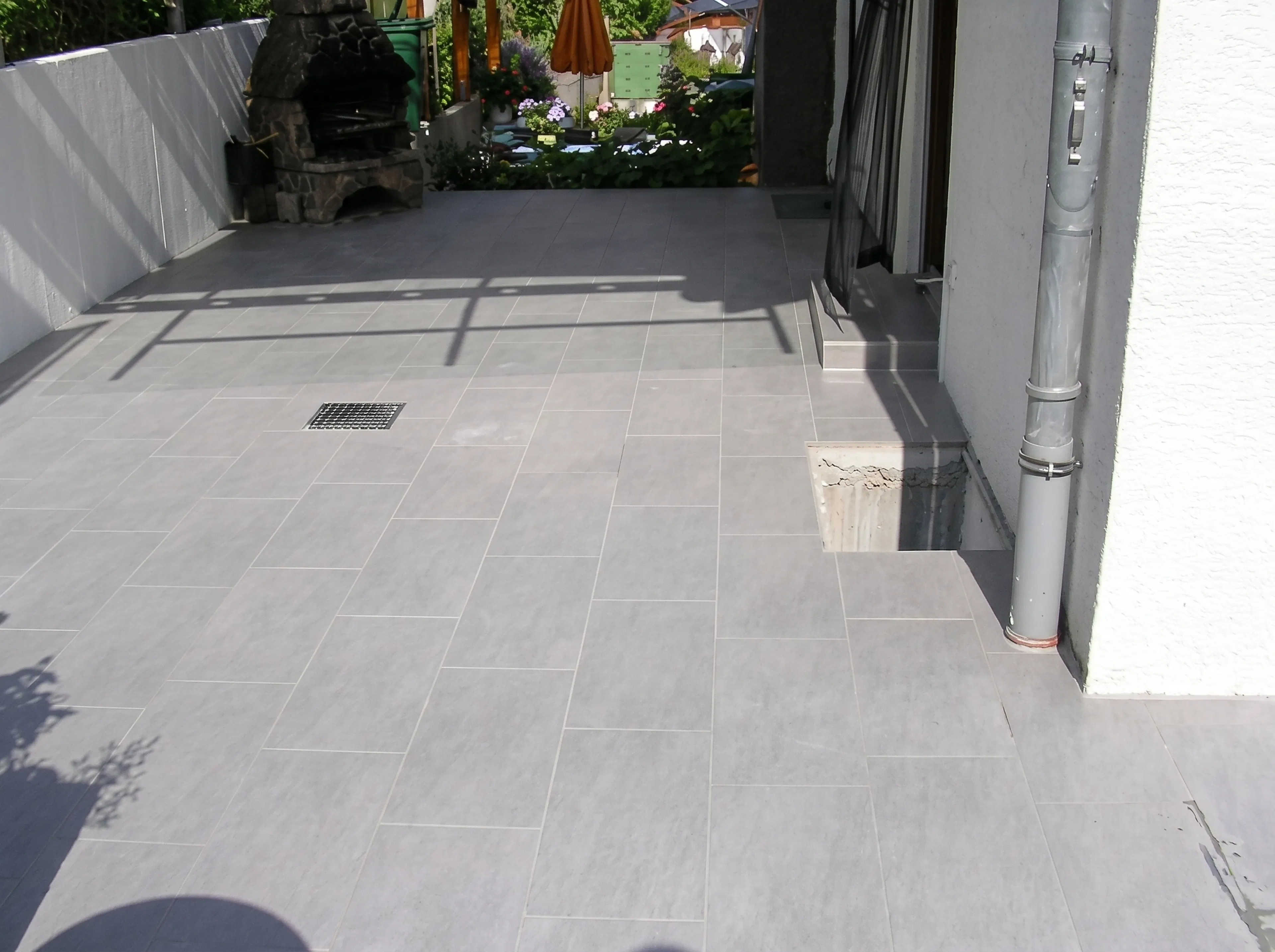 Terrassengestaltung von Fliesen Kurz: Großformatige graue Fliesen auf einer Terrasse mit integriertem Bodenablauf.