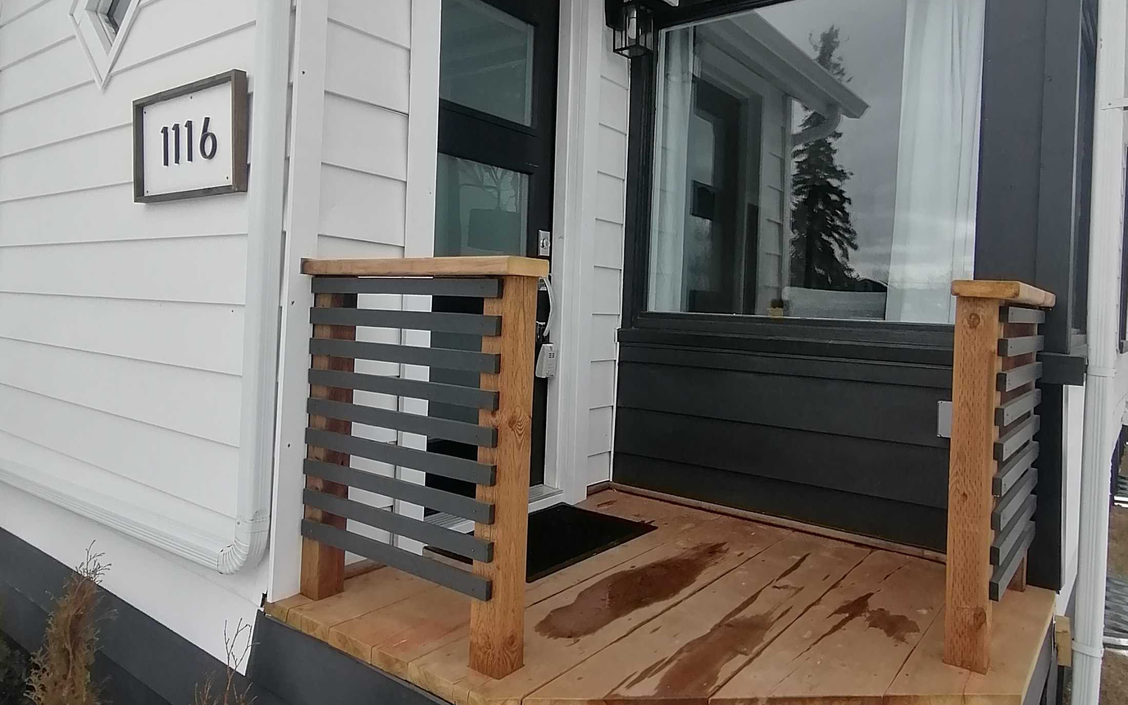 Front door of modern white house with wooden deck and custom siding - Hint of Honey