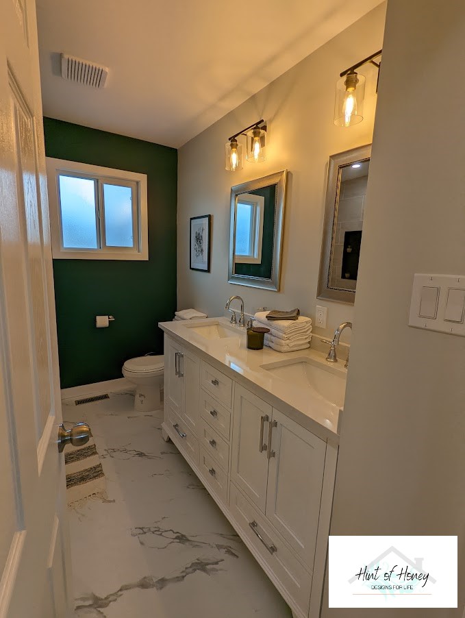 Renovated bathroom with white cabinetry, chic lighting, and marble-like floor, designed by Hint of Honey