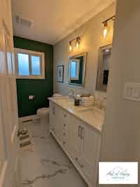 Renovated bathroom with white cabinetry, chic lighting, and marble-like floor, designed by Hint of Honey