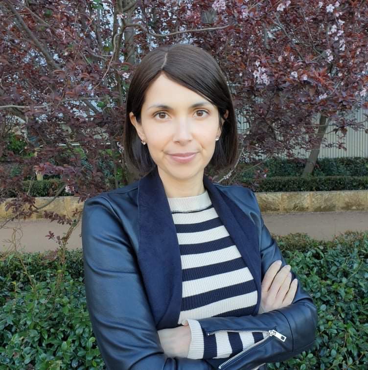 Natalia Hodgins has her arms folded and has short straight brown hair and brown eyes. She is wearing a navy and white striped top and a black leather jacket.