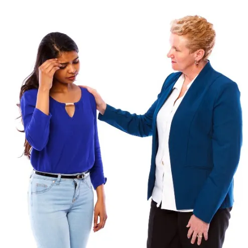 A woman supporting another woman with her hands on her shoulder. The other woman is looking down with her hand on her head.