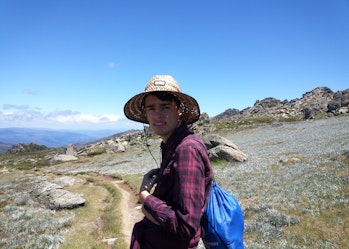 Andrew is on a walking track. He is wearing a large straw hat and a red flannelette shirt.