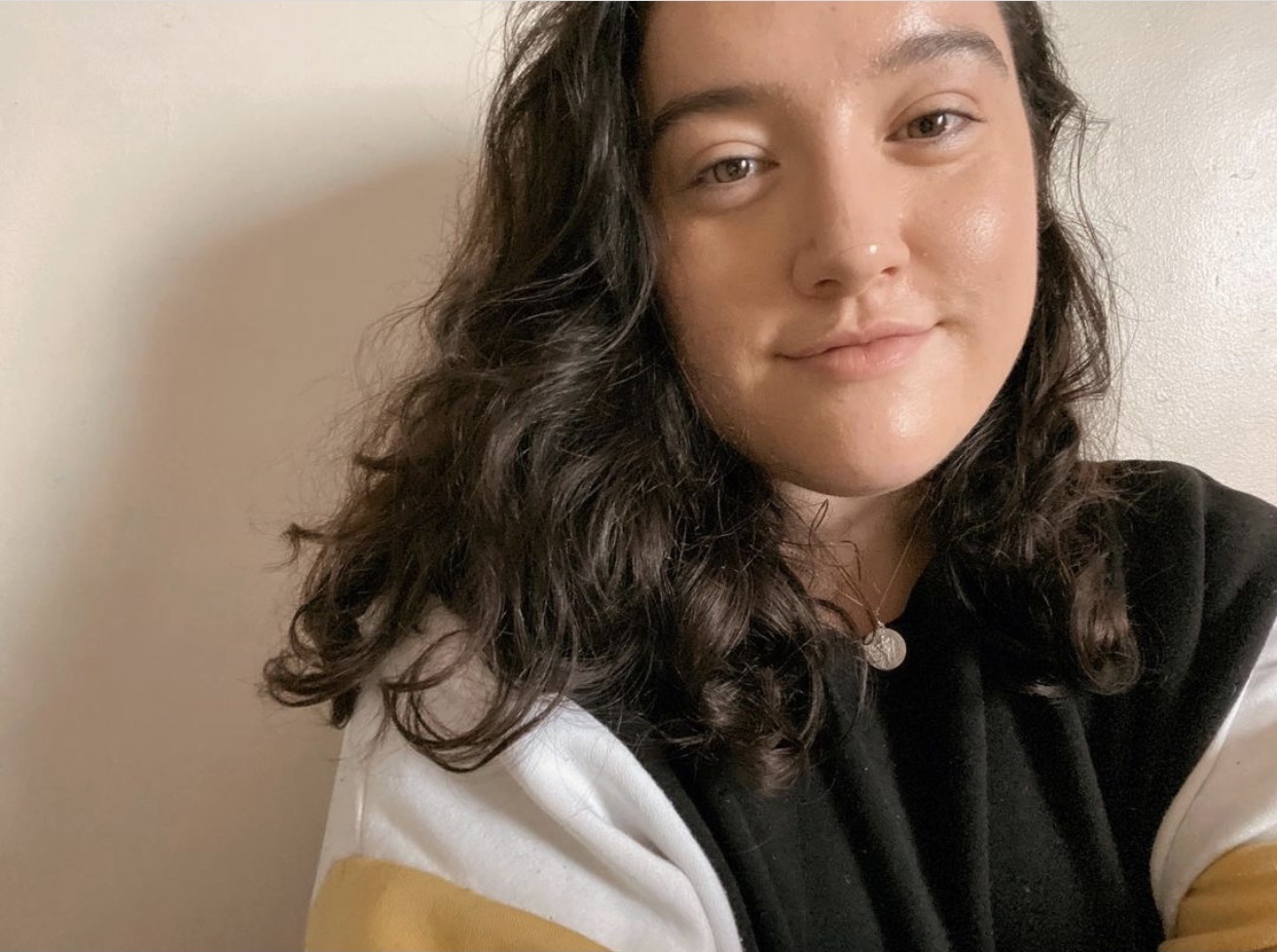 Christin has dark, curly hair and is wearing a pendant necklace. 