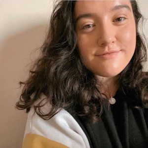 Christin has dark, curly hair and is wearing a pendant necklace.