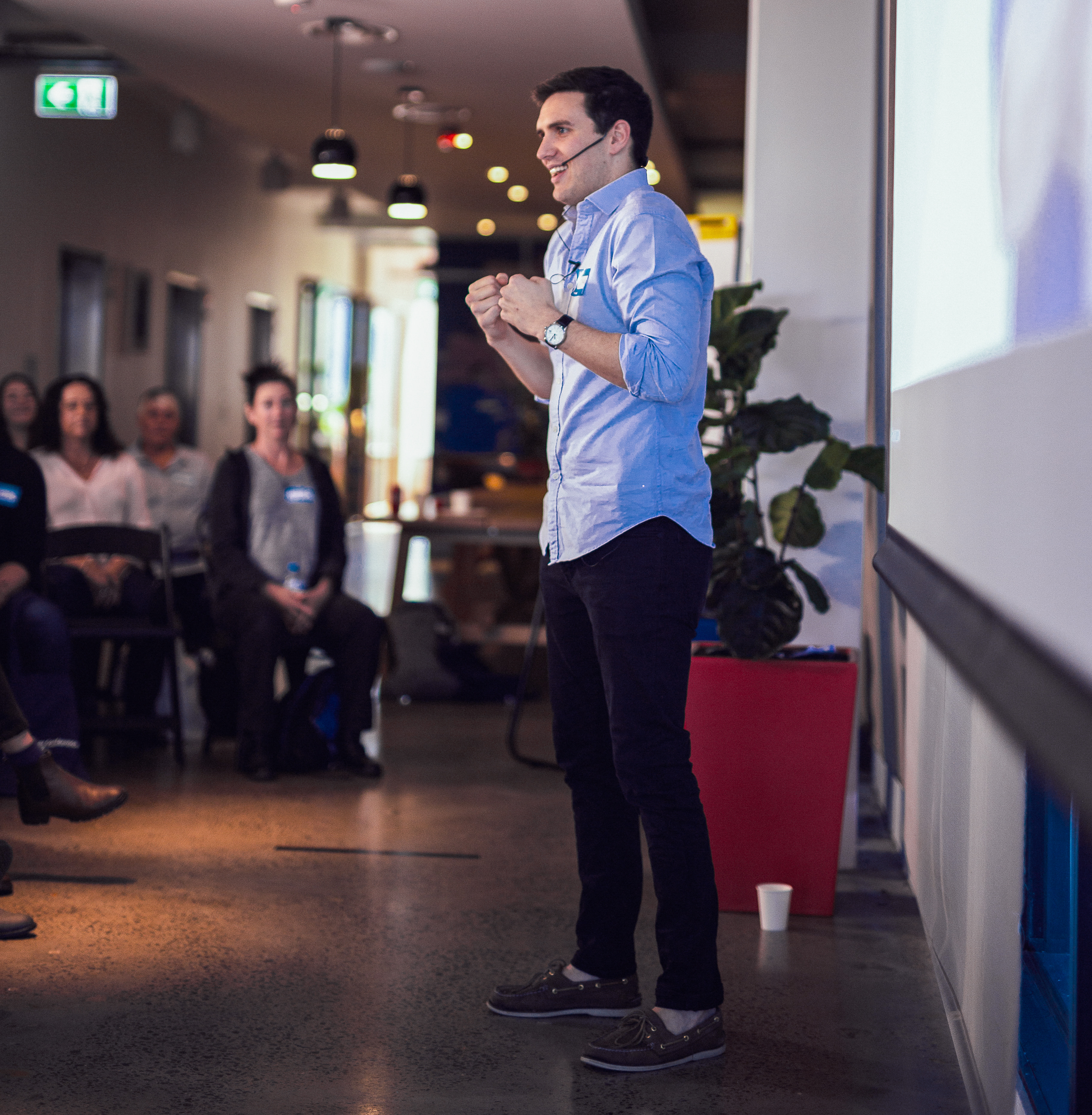 Jordan O'Reilly, Hireup's CEO is talking at a conference. He has a big smile on his face and is wearing a head mic.
