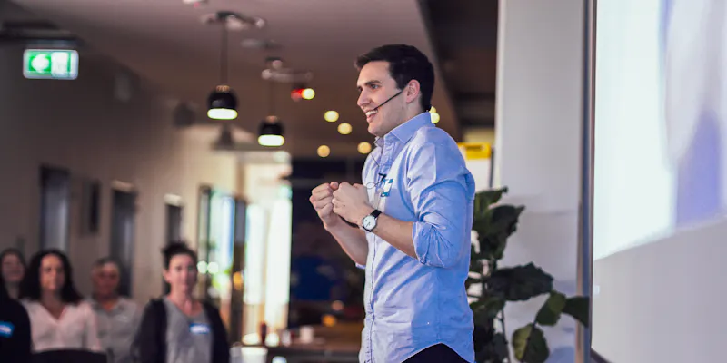 Jordan O'Reilly, Hireup's CEO is talking at a conference. He has a big smile on his face and is wearing a head mic.