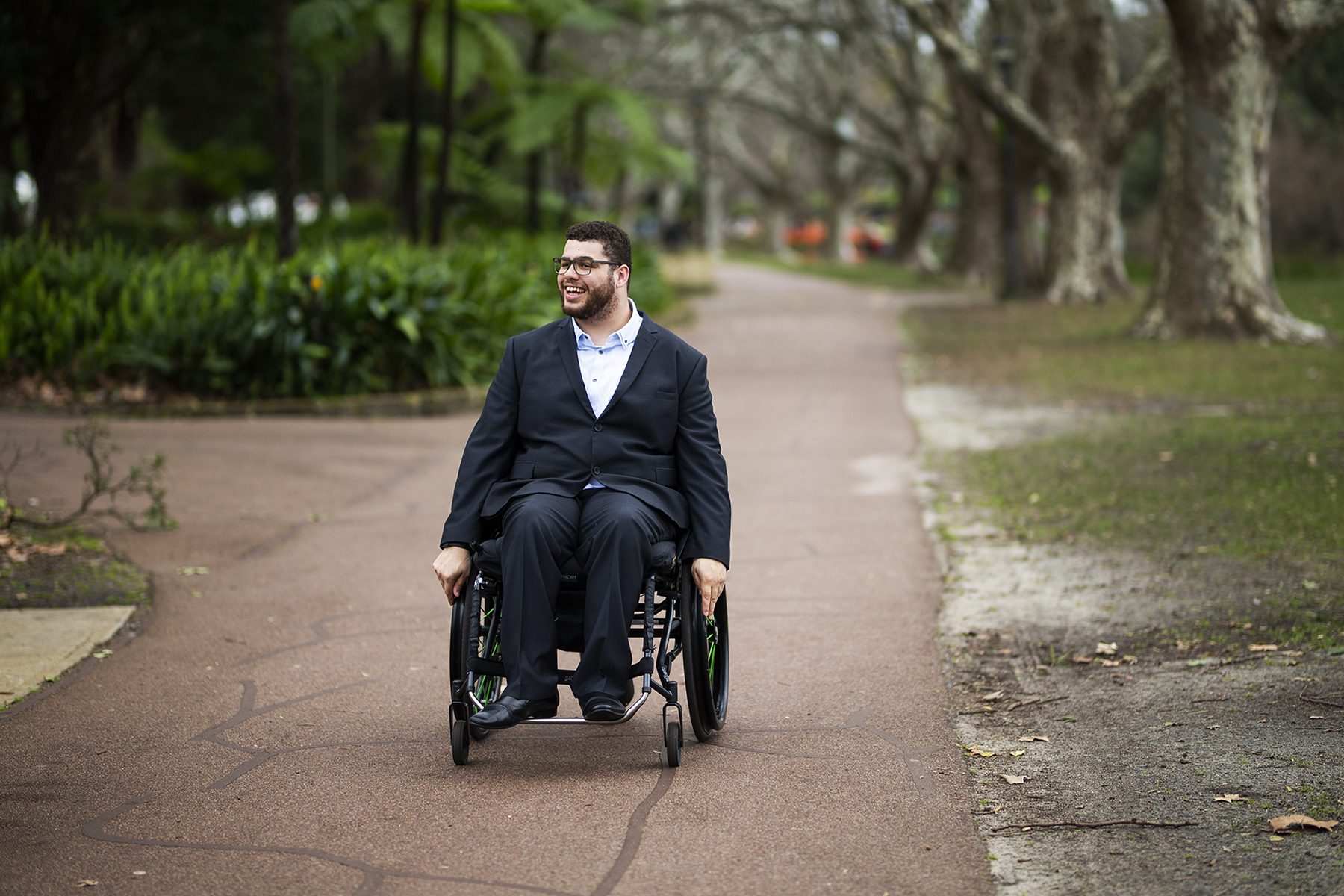 Senator Jordon Steele-John is sitting in a wheelchair, in a park, smiling. 